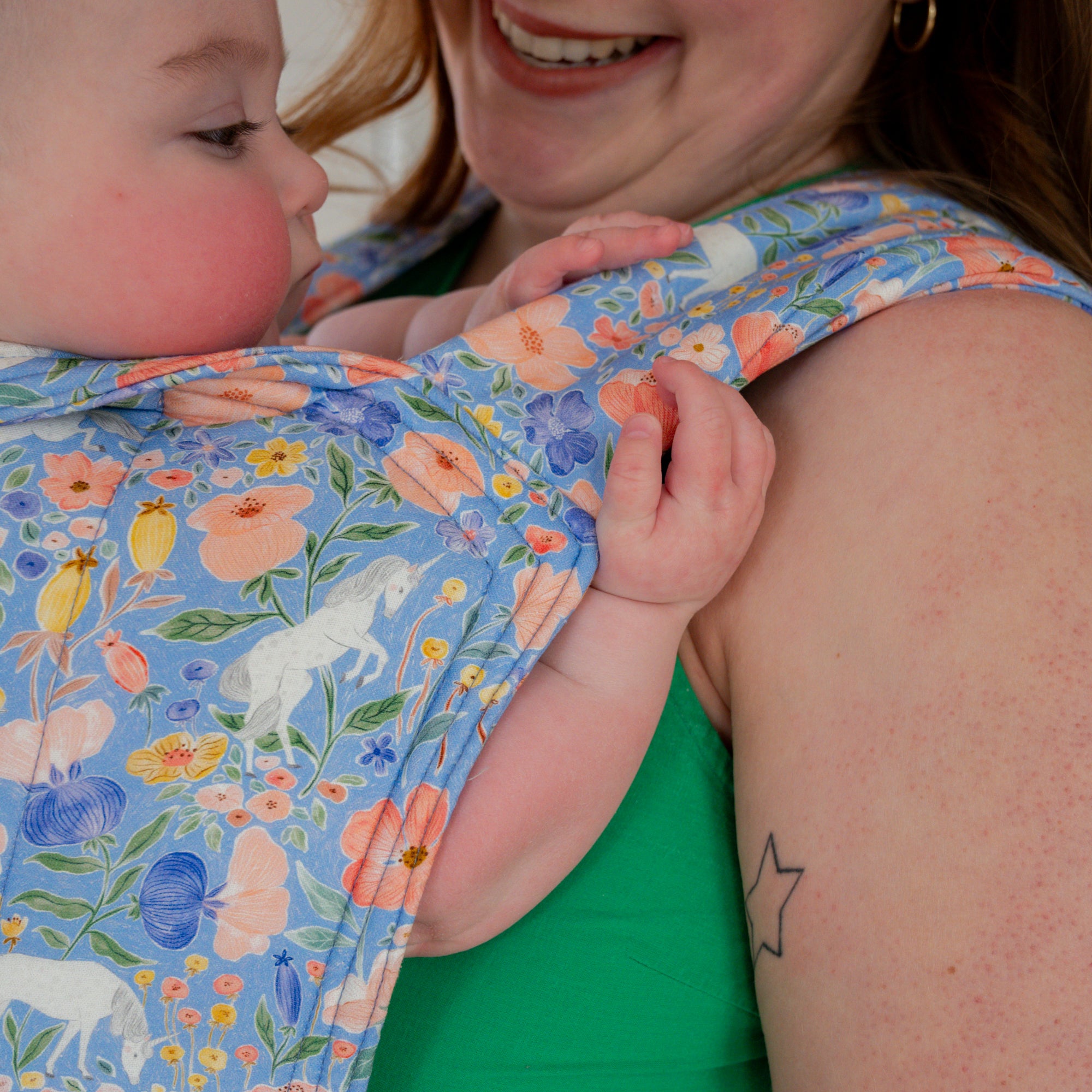 Woman carrying a baby in a floral unicorn patterned carrier.