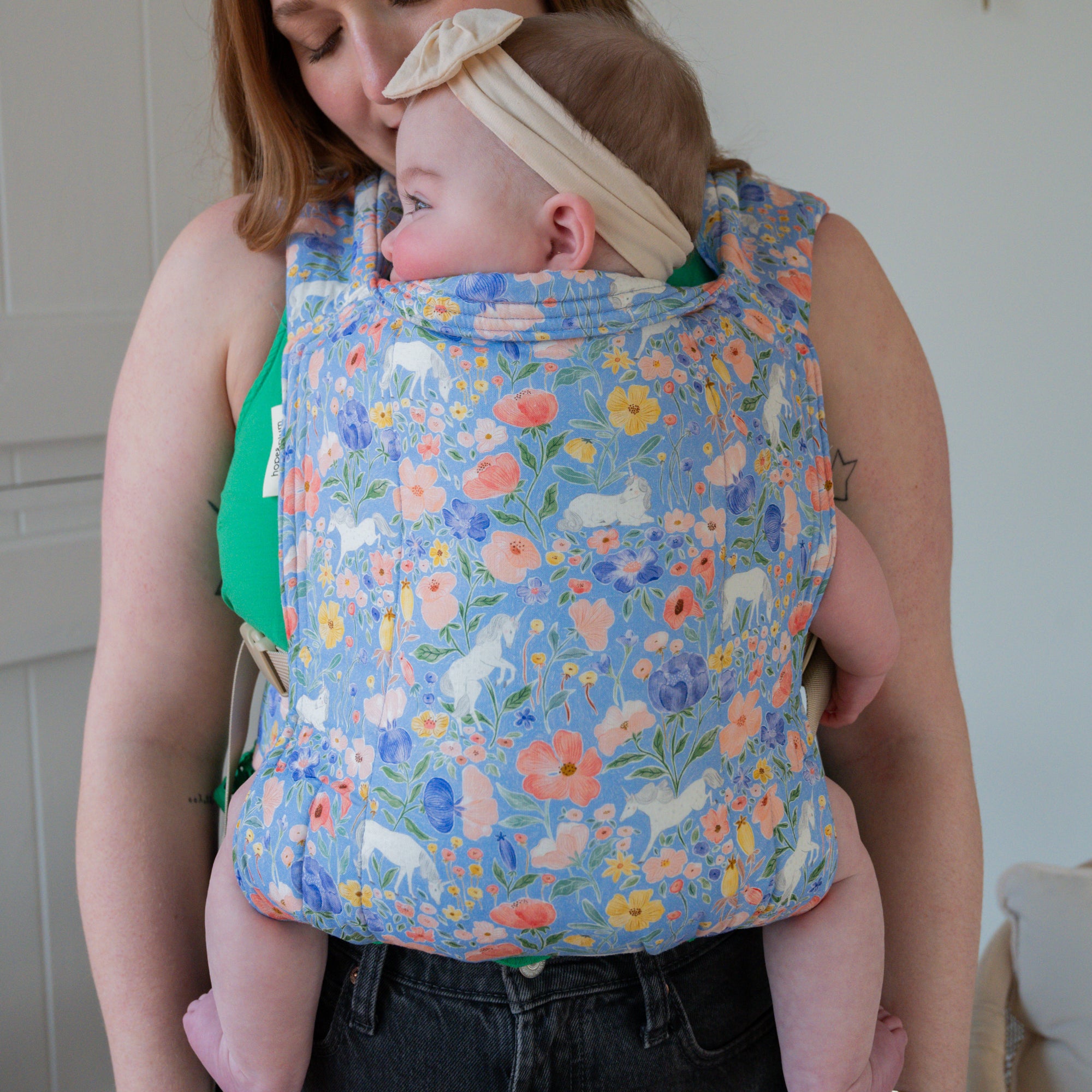 Woman carrying a baby in a floral unicorn patterned carrier.