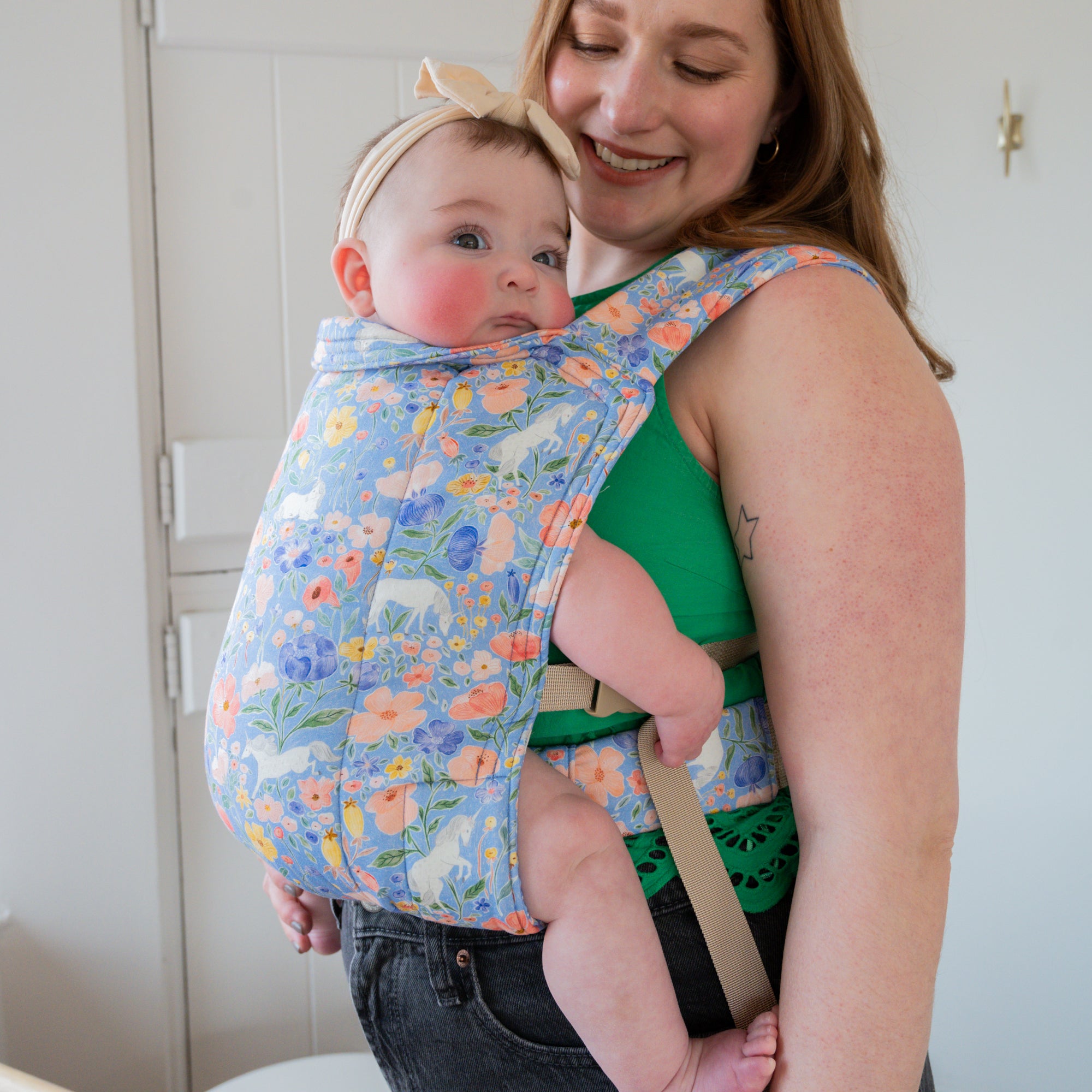 Woman carrying a baby in a floral unicorn patterned carrier.