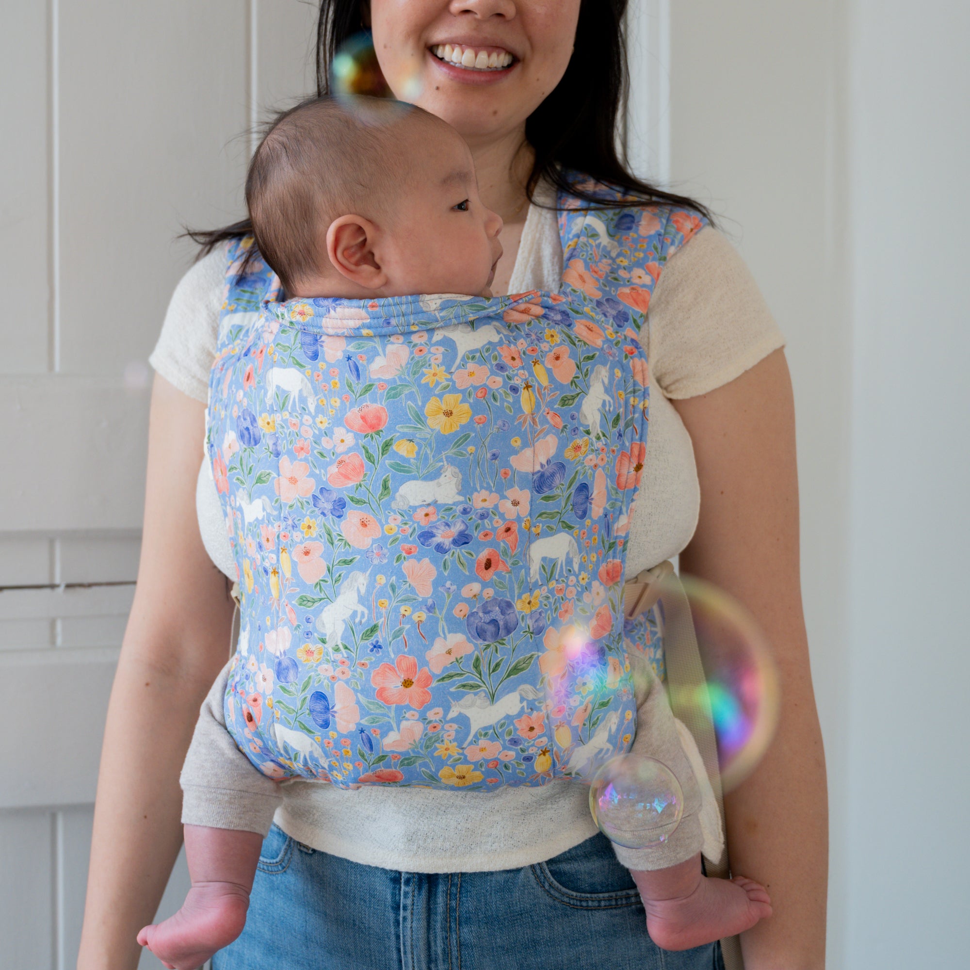 Woman carrying a baby in a floral unicorn patterned carrier.