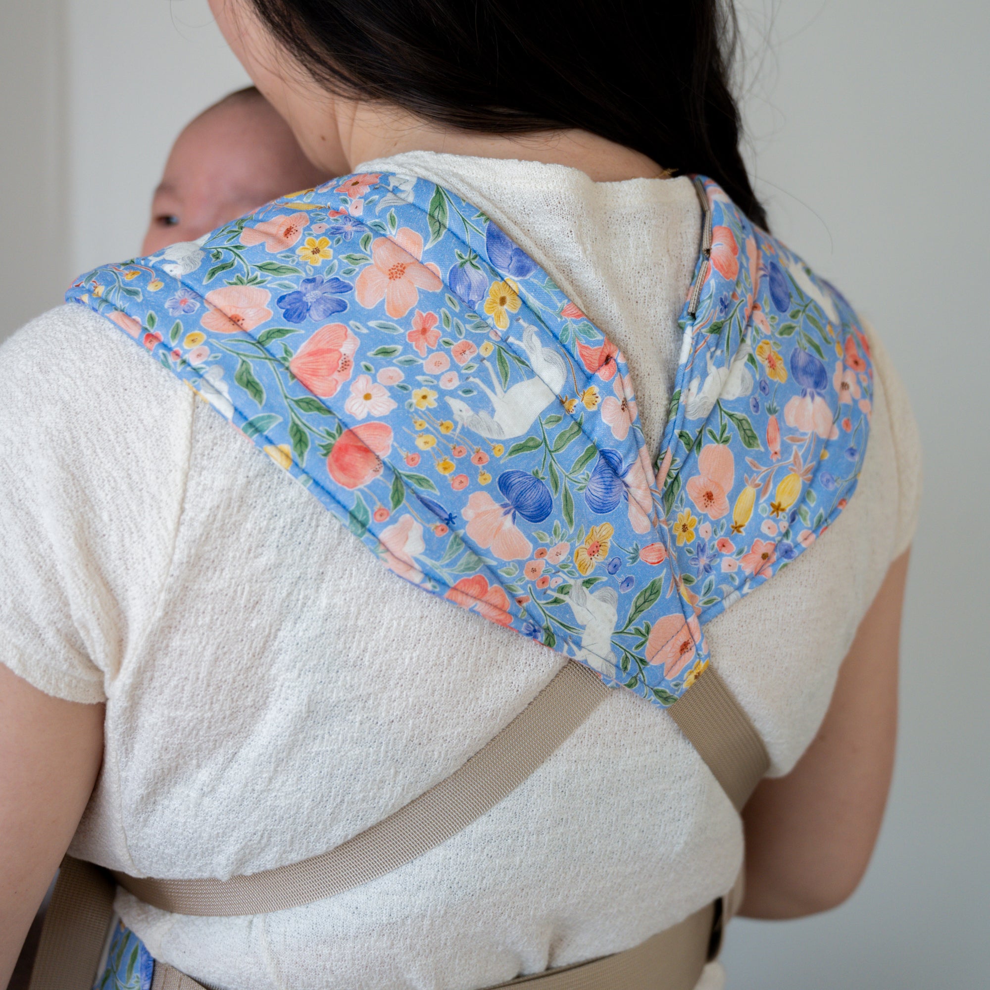 Woman carrying a baby in a floral unicorn patterned carrier.