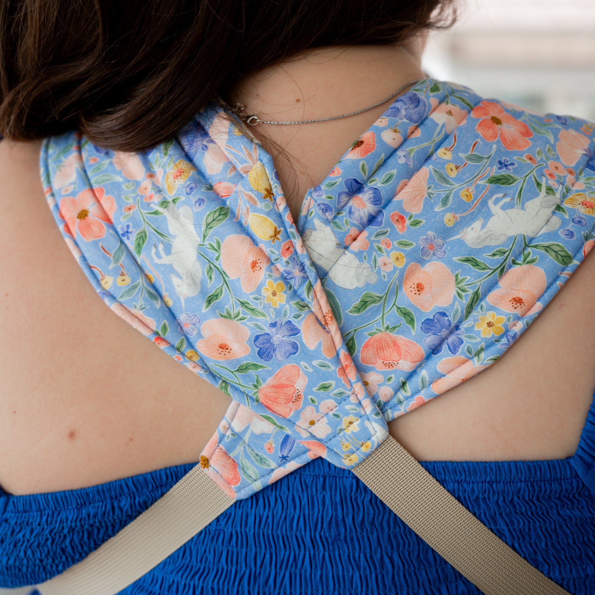Woman carrying a baby in a floral unicorn patterned carrier.