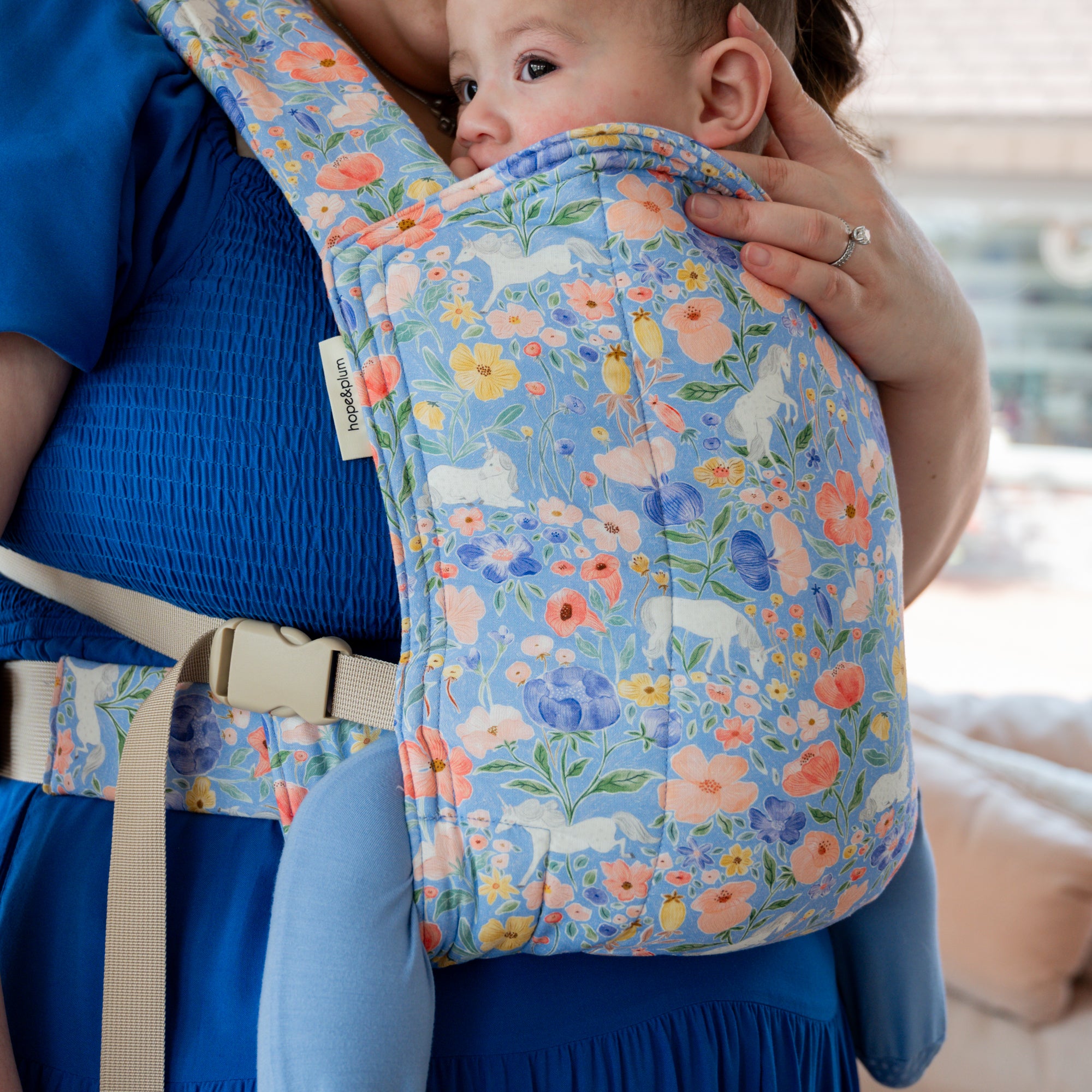 Baby in a floral unicorn baby carrier with a blurred indoor background