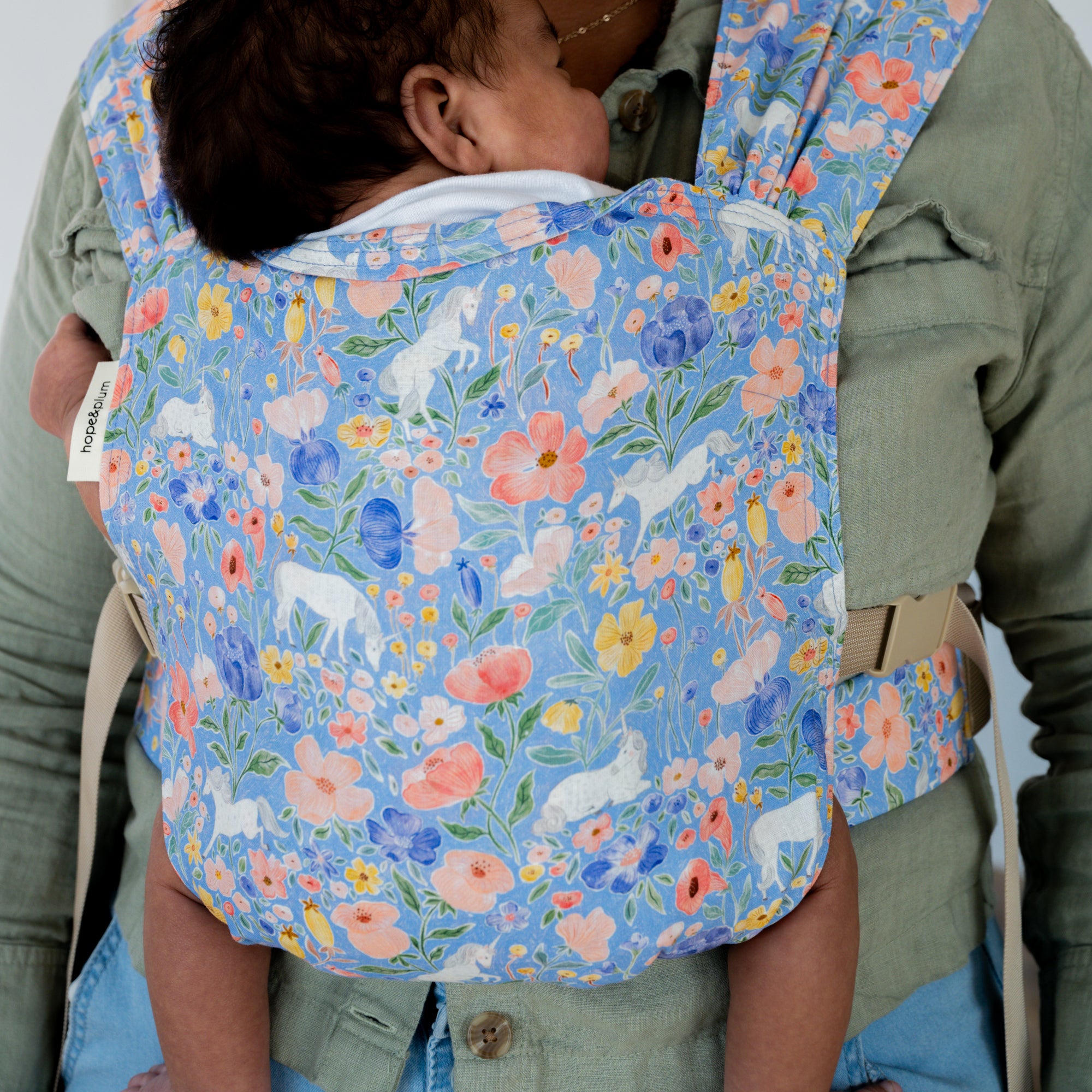 Child in a floral unicorn baby carrier with unicorns and flowers.
