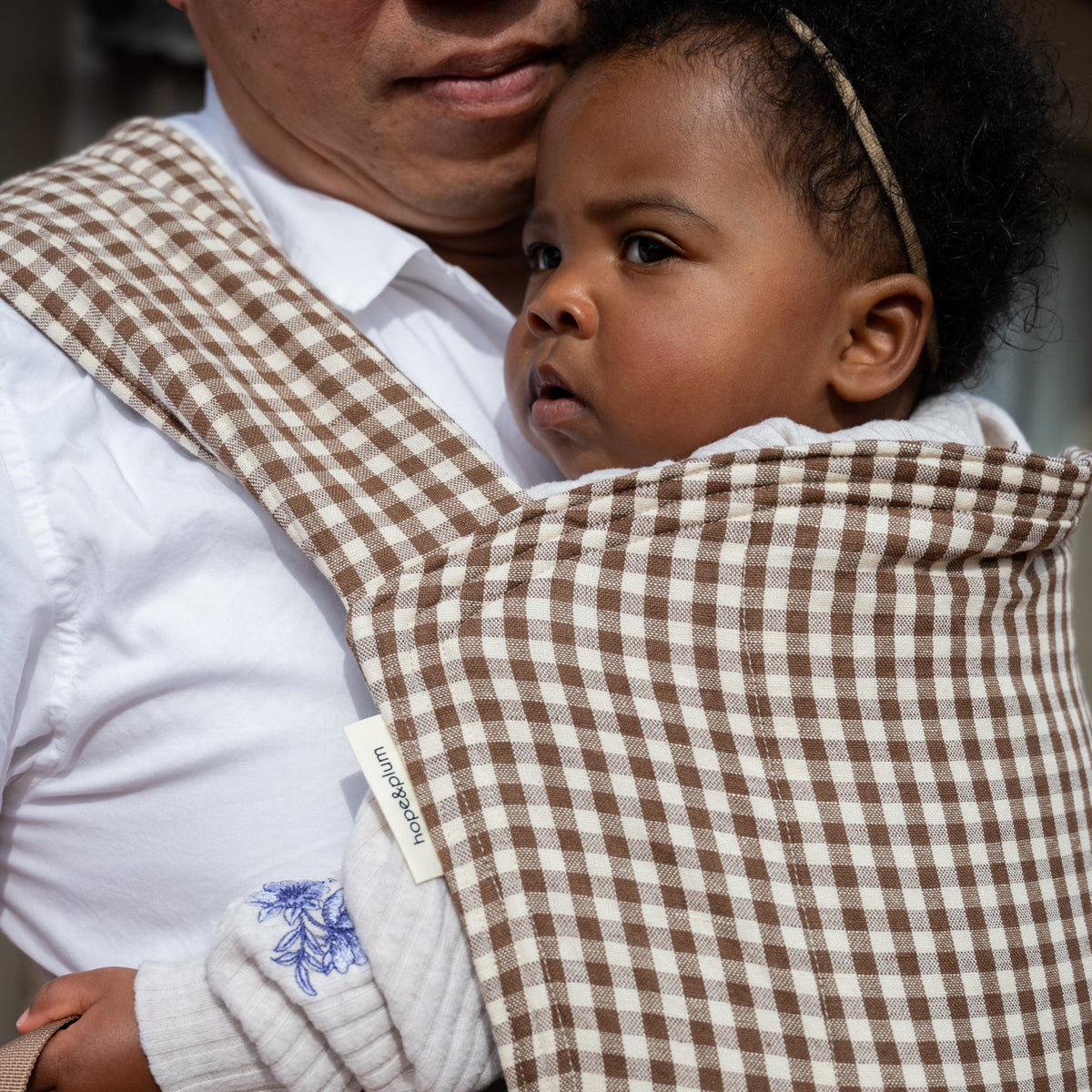 Lark Baby Carrier in Clove — close-up of a toddler resting against the gingham hood, caregiver smiling down at her.