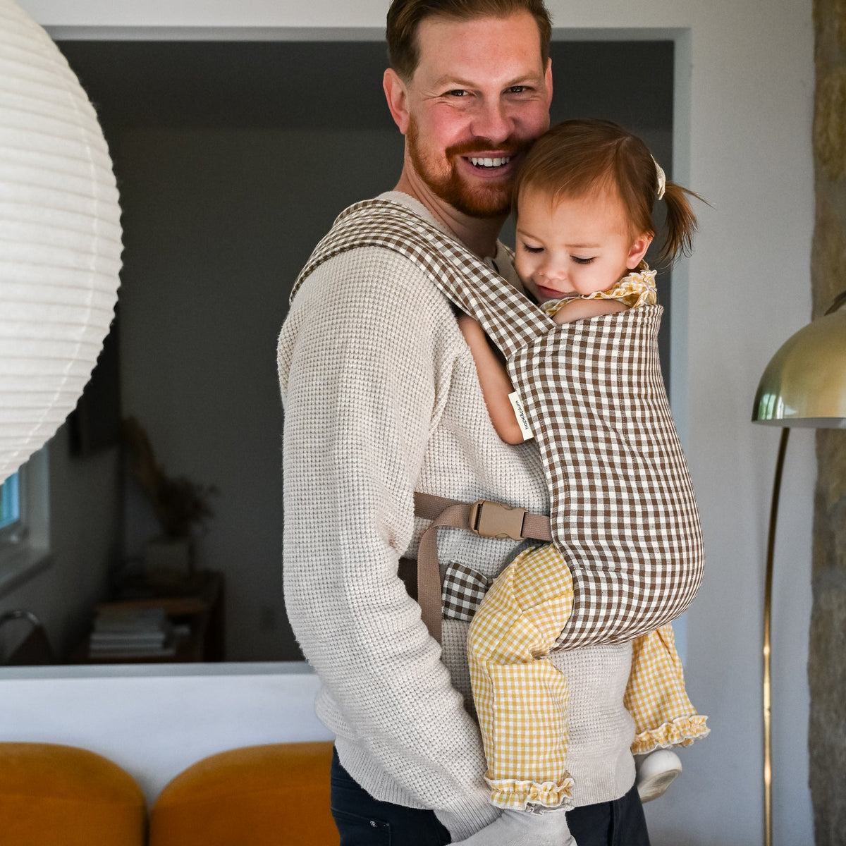 Lark Baby Carrier in Clove — caregiver resting his cheek against a toddler's head, gingham carrier at his shoulder.