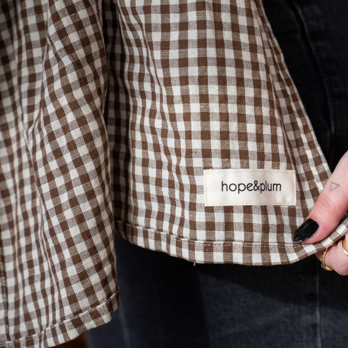 Ring Sling in Clove — close-up of the gingham hem and hope&plum label, caregiver's hand resting on the fabric.