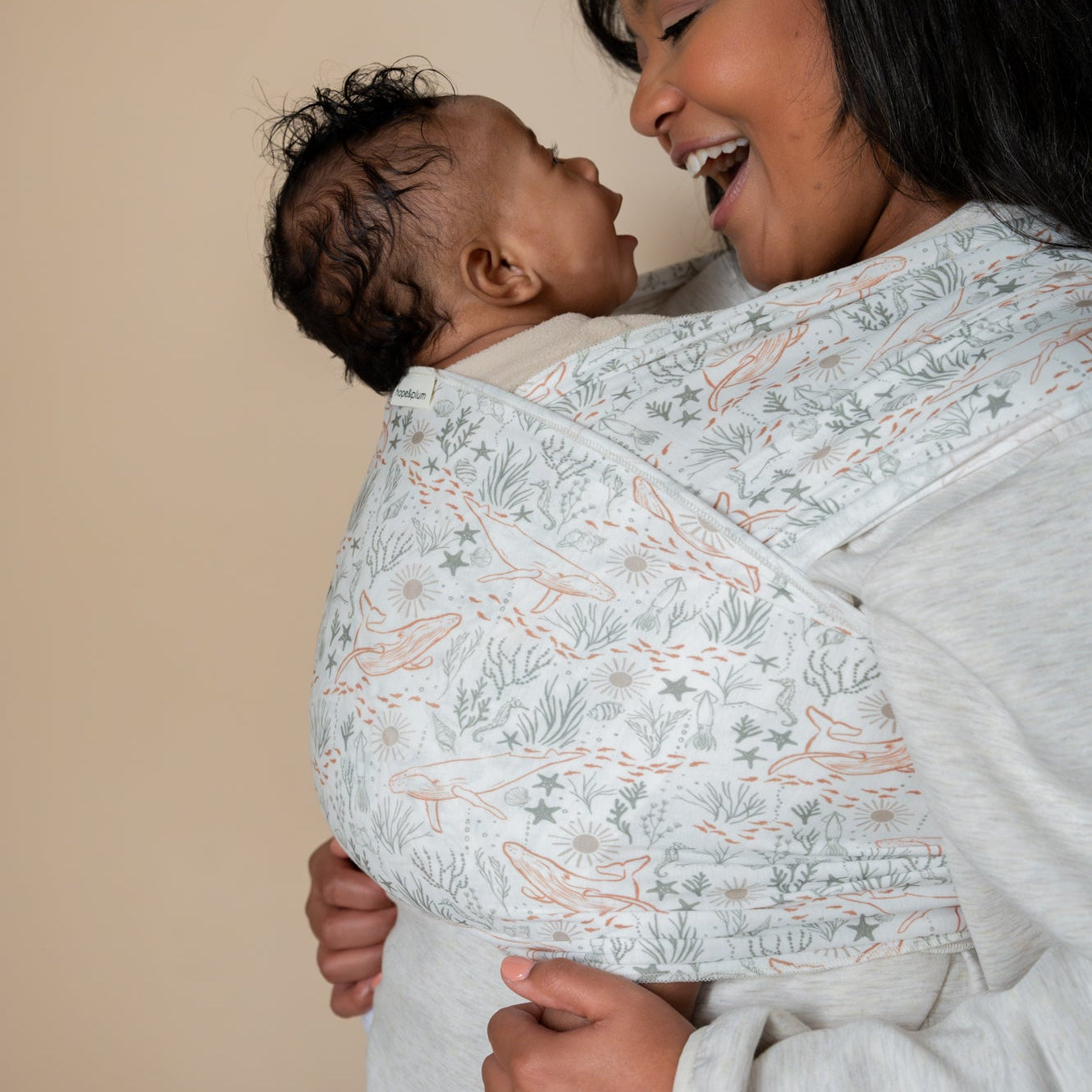 Woman holding a baby in a ocean print wrap, both smiling indoors.