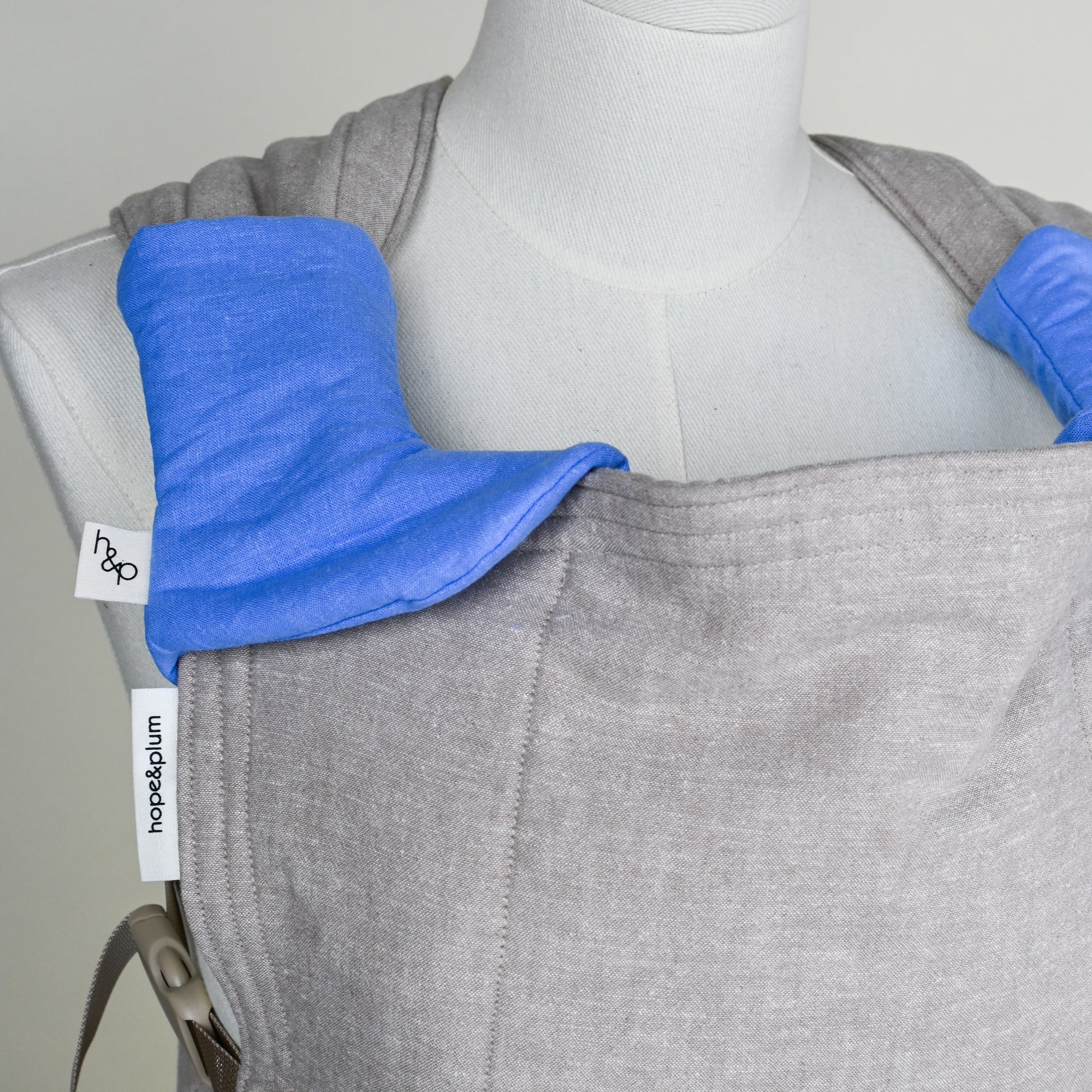 greige baby carrier with blue drool pads on a mannequin, featuring 'hope&plum' label.