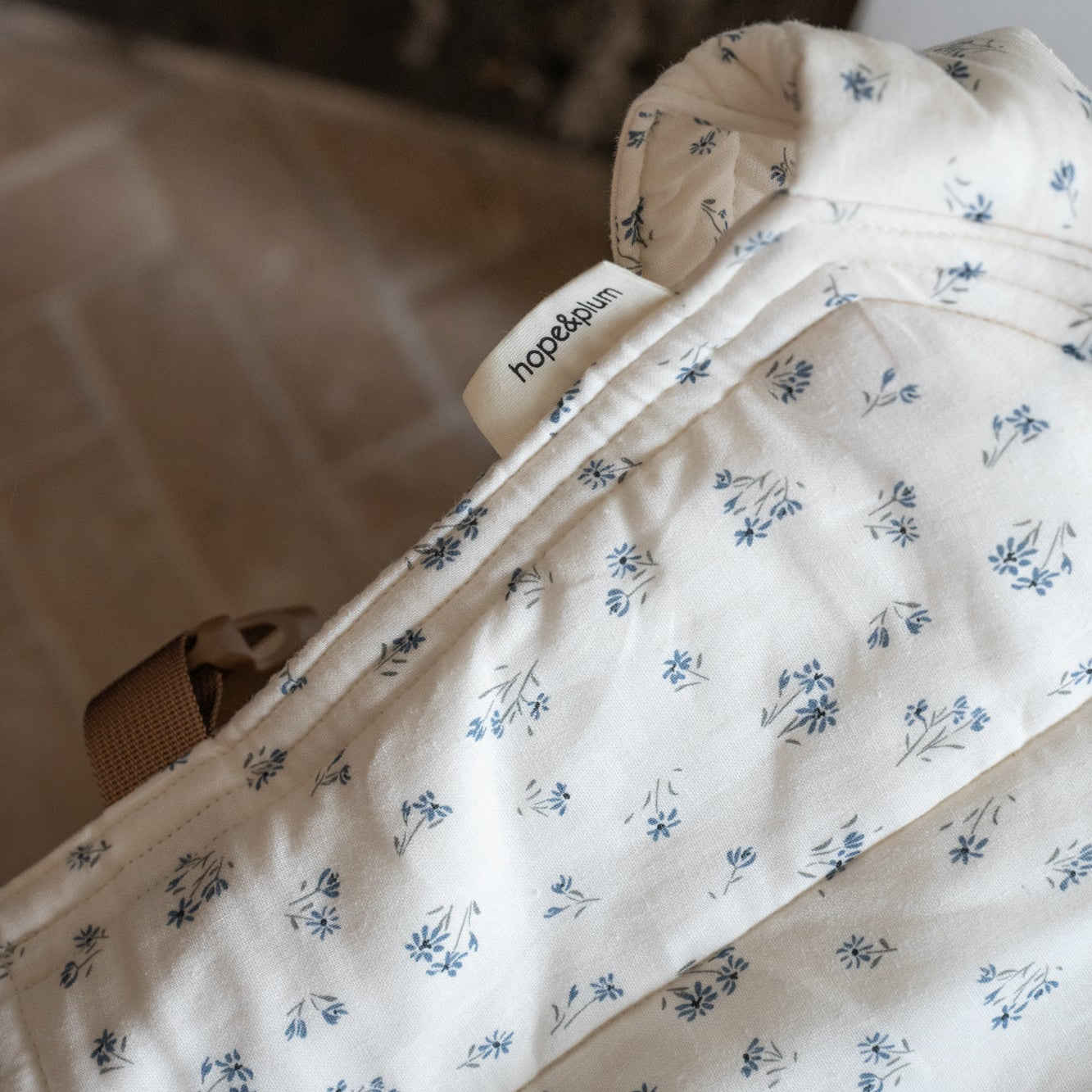 Floral-patterned baby carrier with 'hope&plum' branding on a blurred background