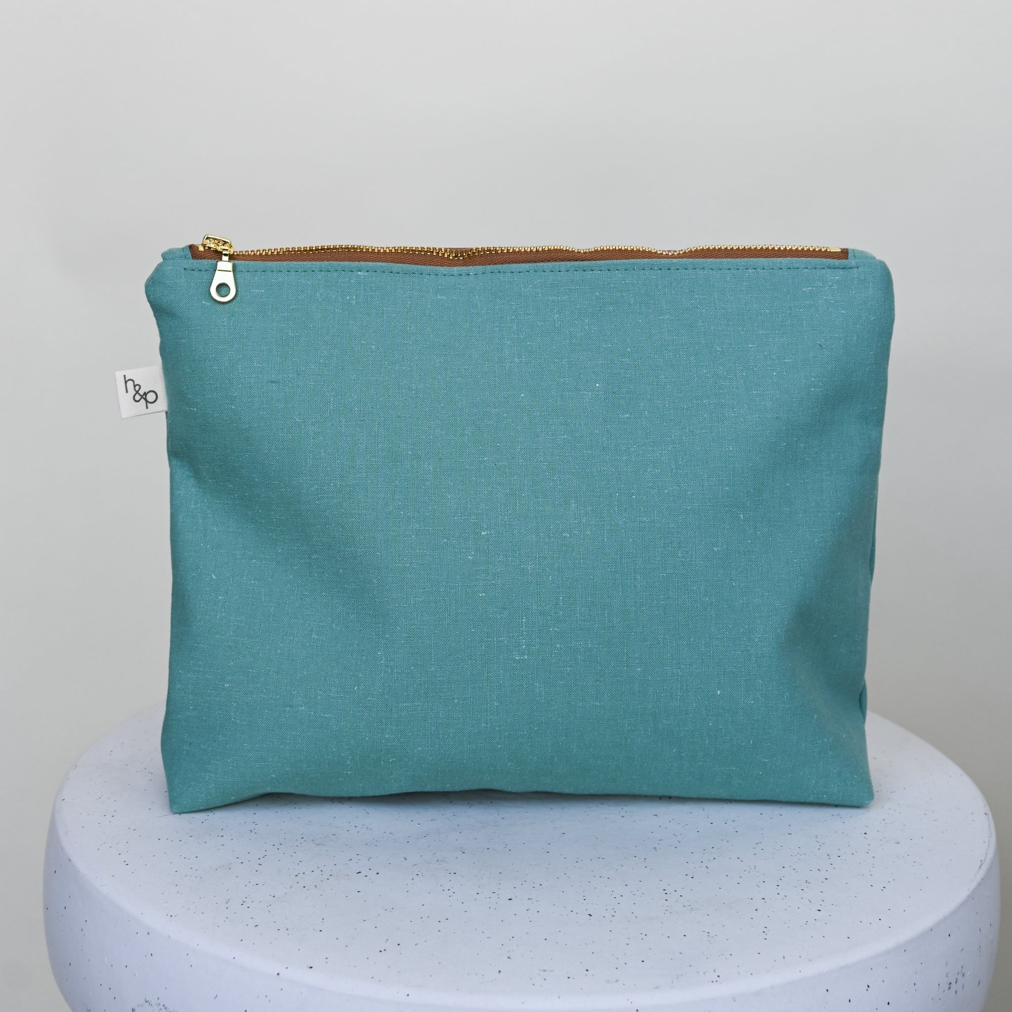 green pouch with gold zipper on a white pedestal against a light gray background