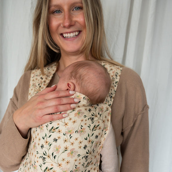 Woman holding a baby in a floral baby carrier against a white background