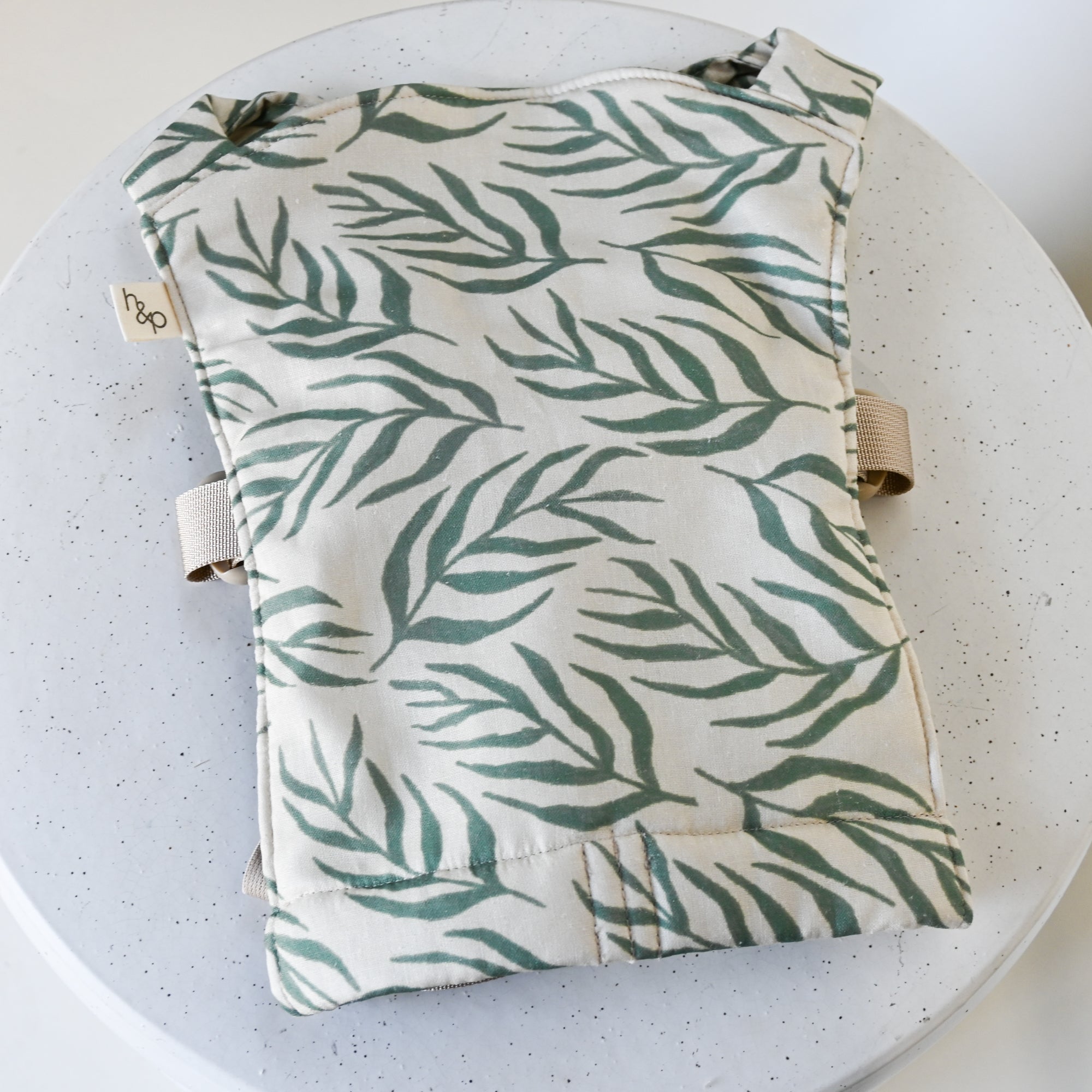 Baby doll carrier with green leaf pattern on a white background