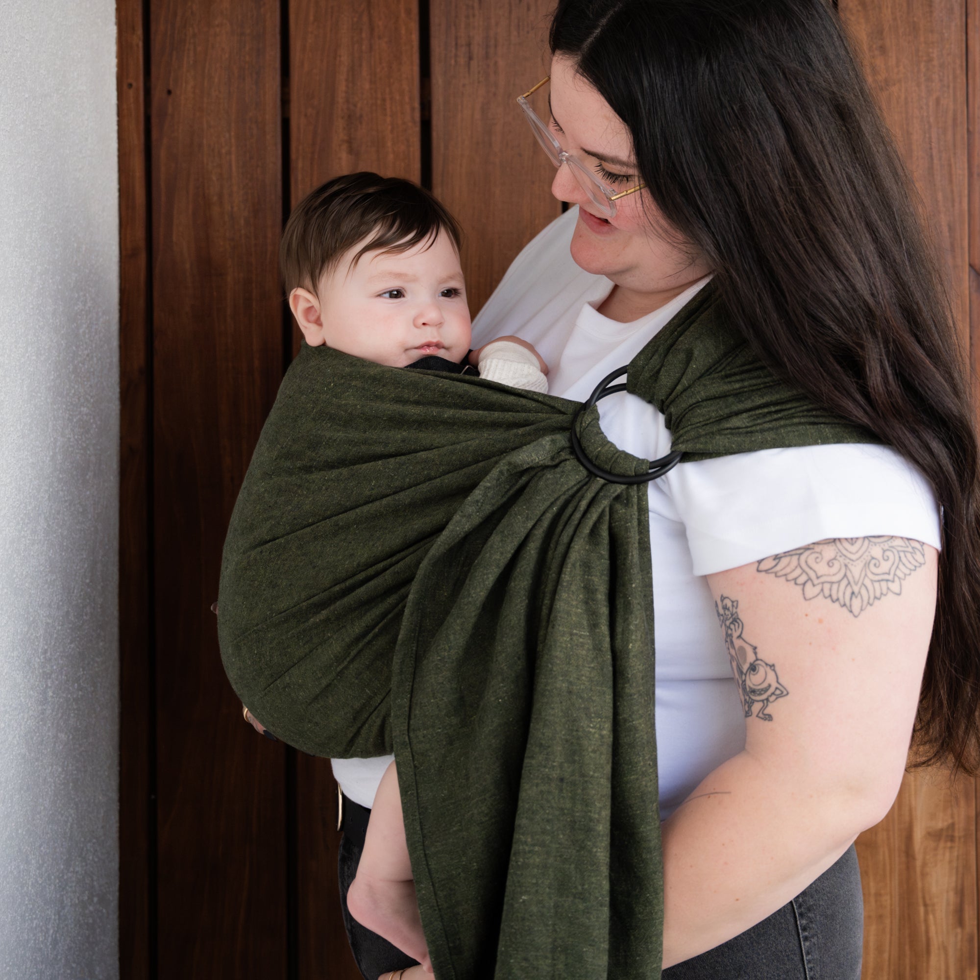 Woman holding a baby in a green sling against a wooden background