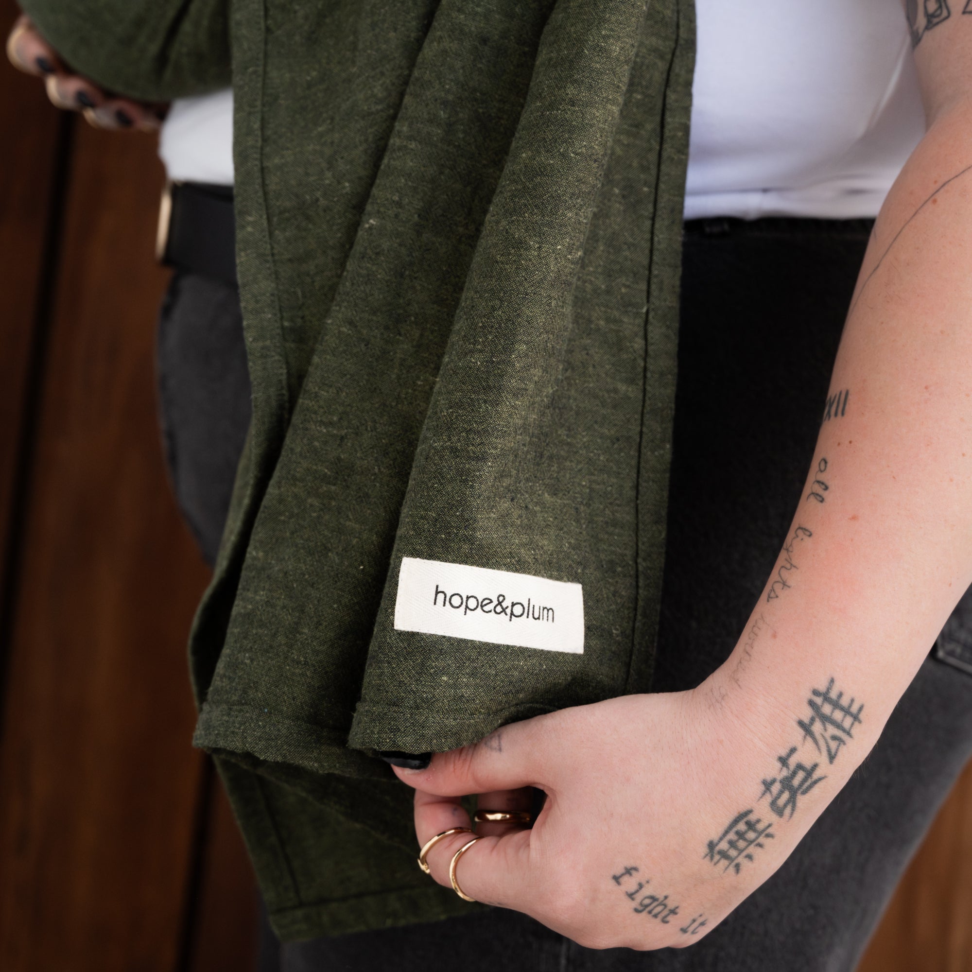 Person holding a green ring sling tail with 'hope&plum' label, tattooed arm visible