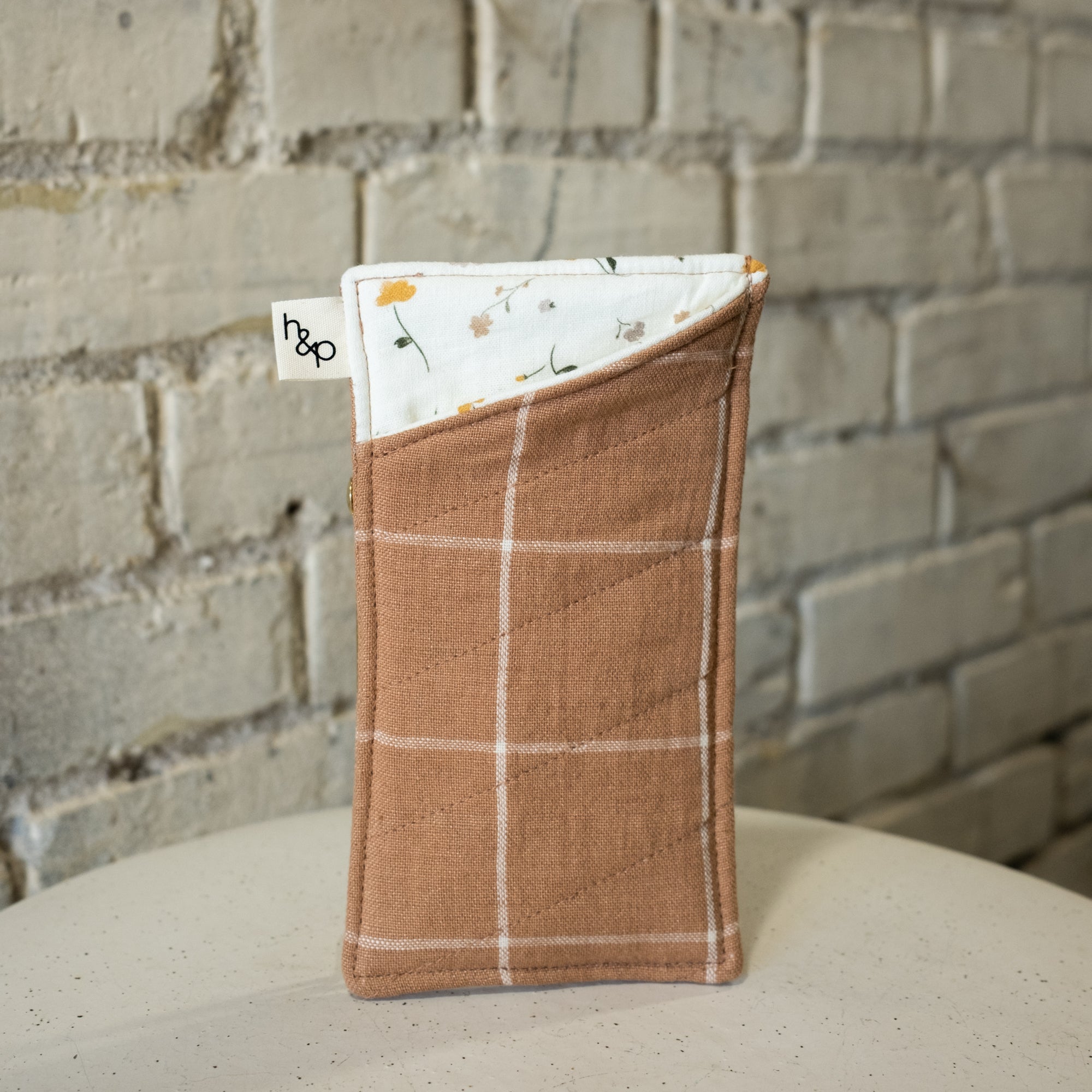 Fabric pouch with plaid pattern on a surface against a brick wall background