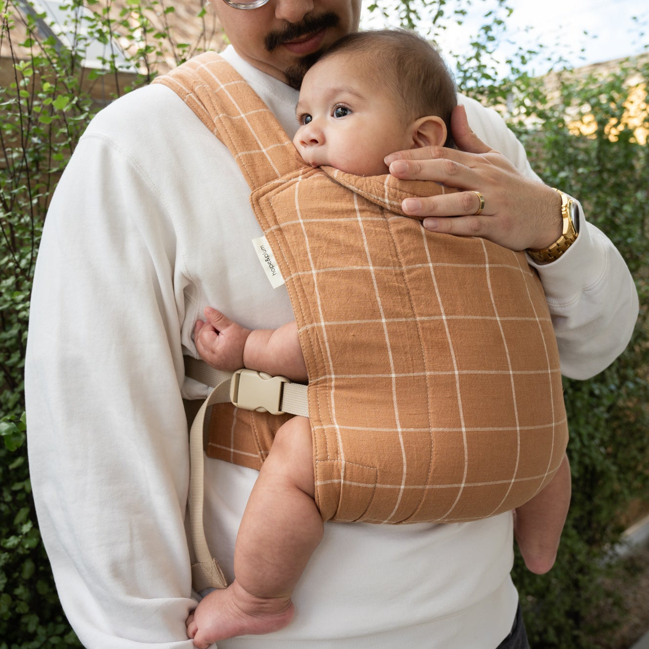 Man holding a baby in a brown grid-patterned carrier