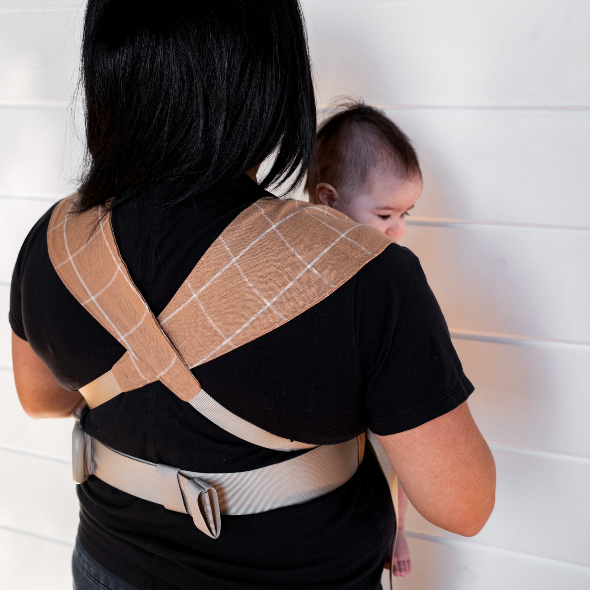 Woman holding a baby in a brown baby carrier with a white grid against a white background
