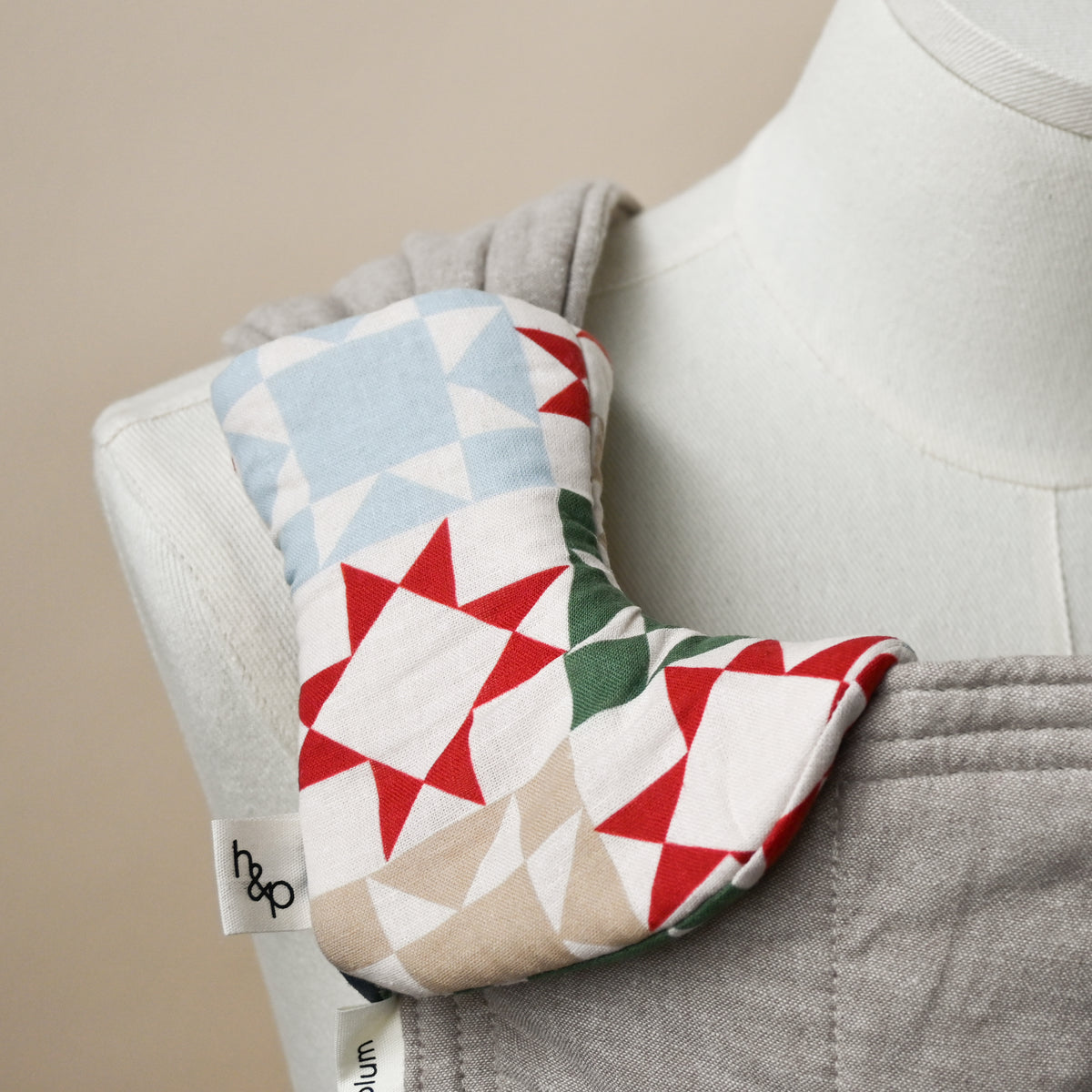 Drool Pads in Heirloom, wrapped over a carrier shoulder strap on a dress form, cream fabric printed with patchwork quilt star blocks in red, green, navy, slate blue and taupe.