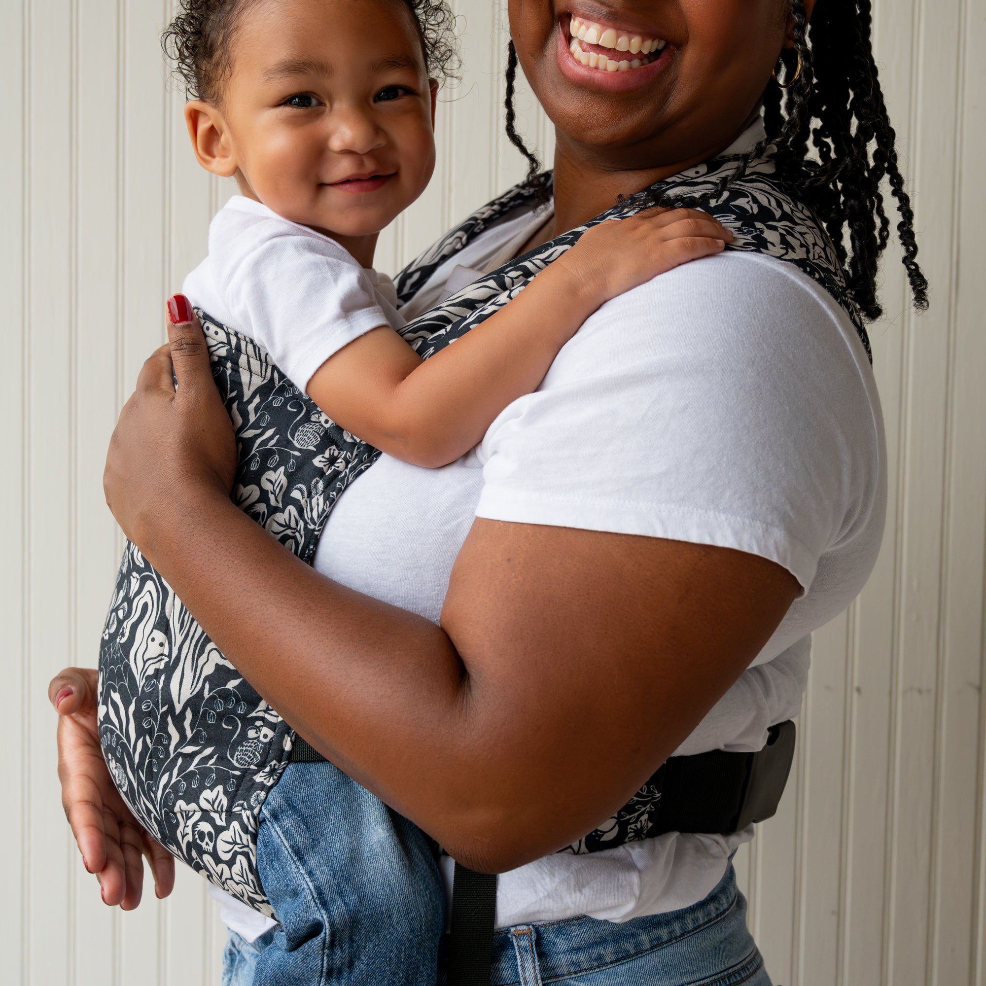 Woman holding a child in a baby buckle carrier against a white wall