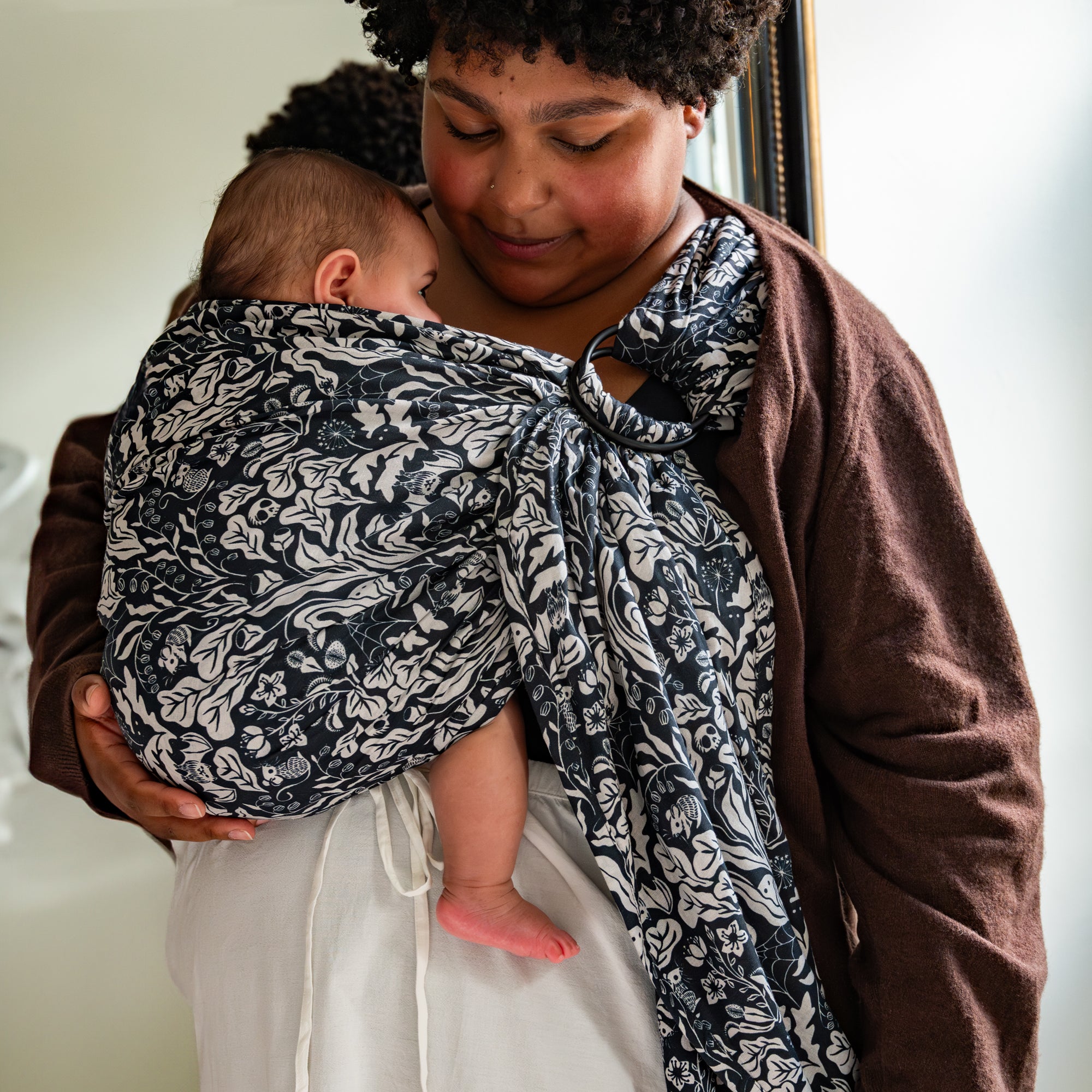 Person holding a baby wrapped in a patterned wrap sling carrier against a neutral background