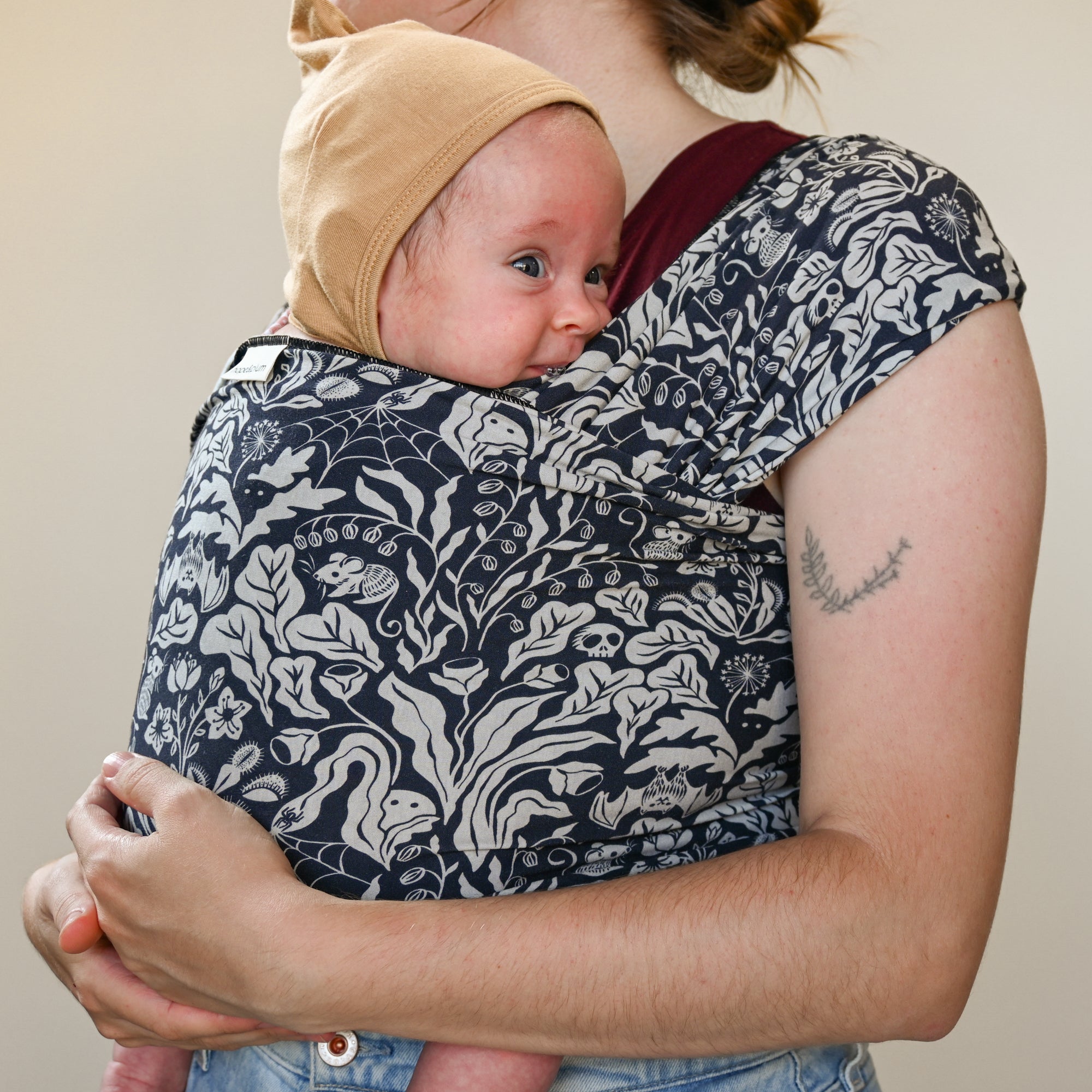 Person holding a baby in a floral-patterned sling against a neutral background