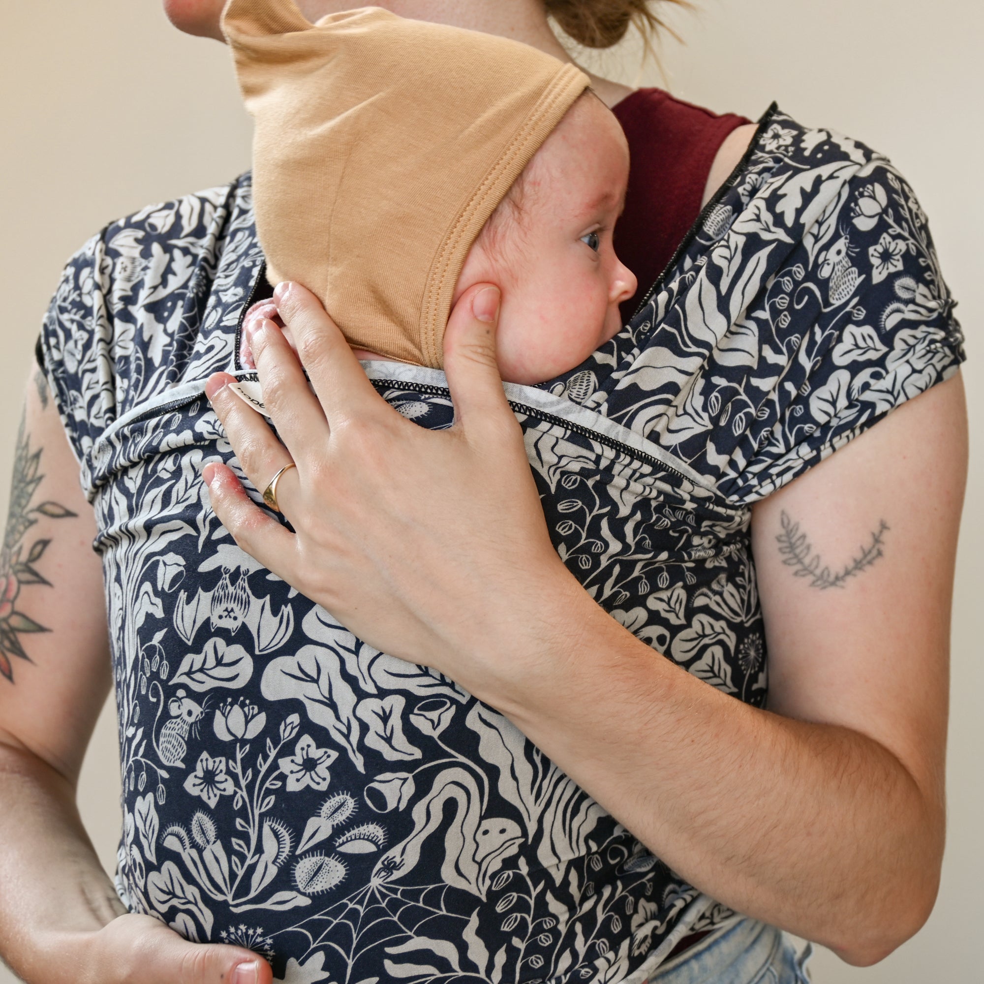 Person holding a baby in a floral-patterned sling against a neutral background
