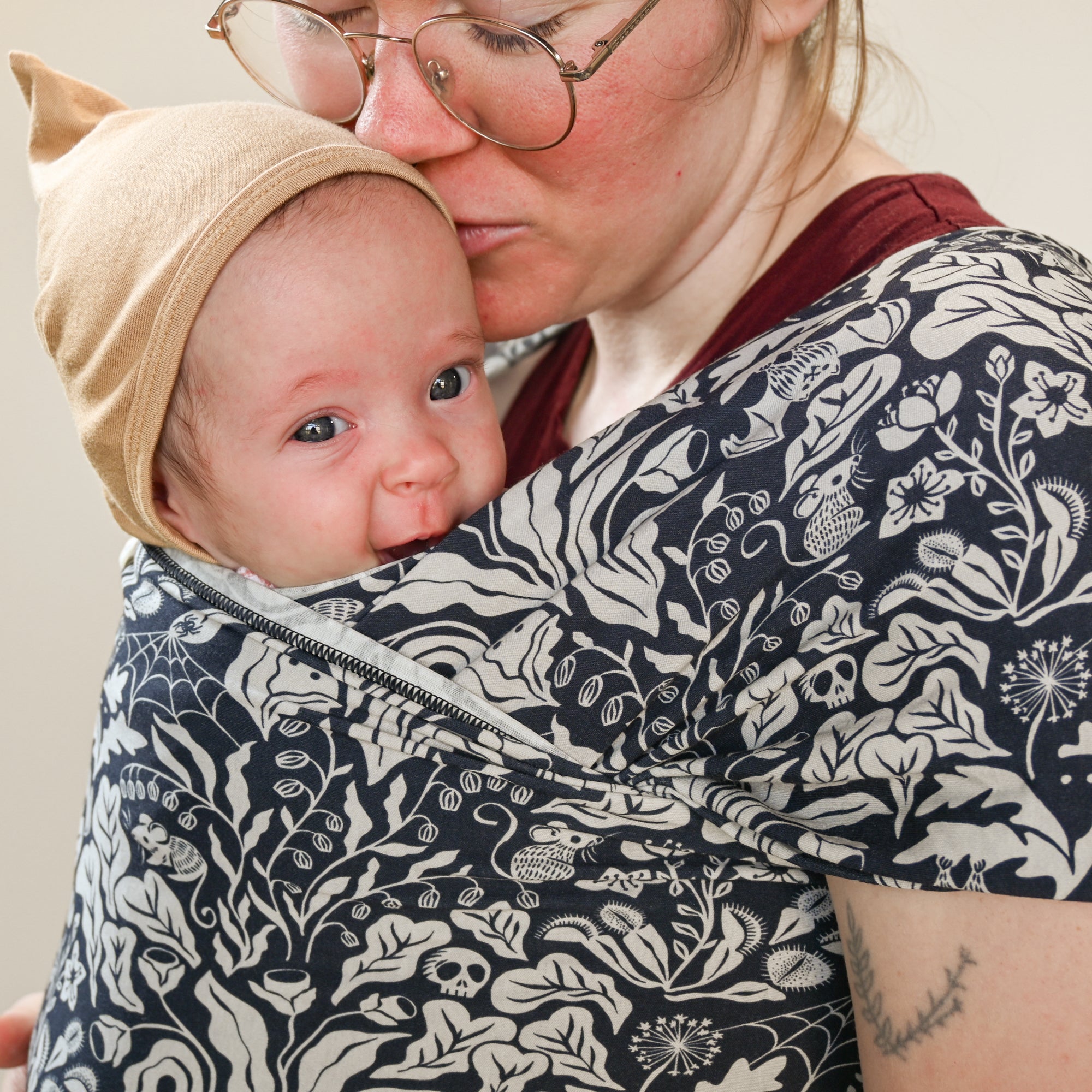 Person holding a baby in a floral-patterned sling against a neutral background