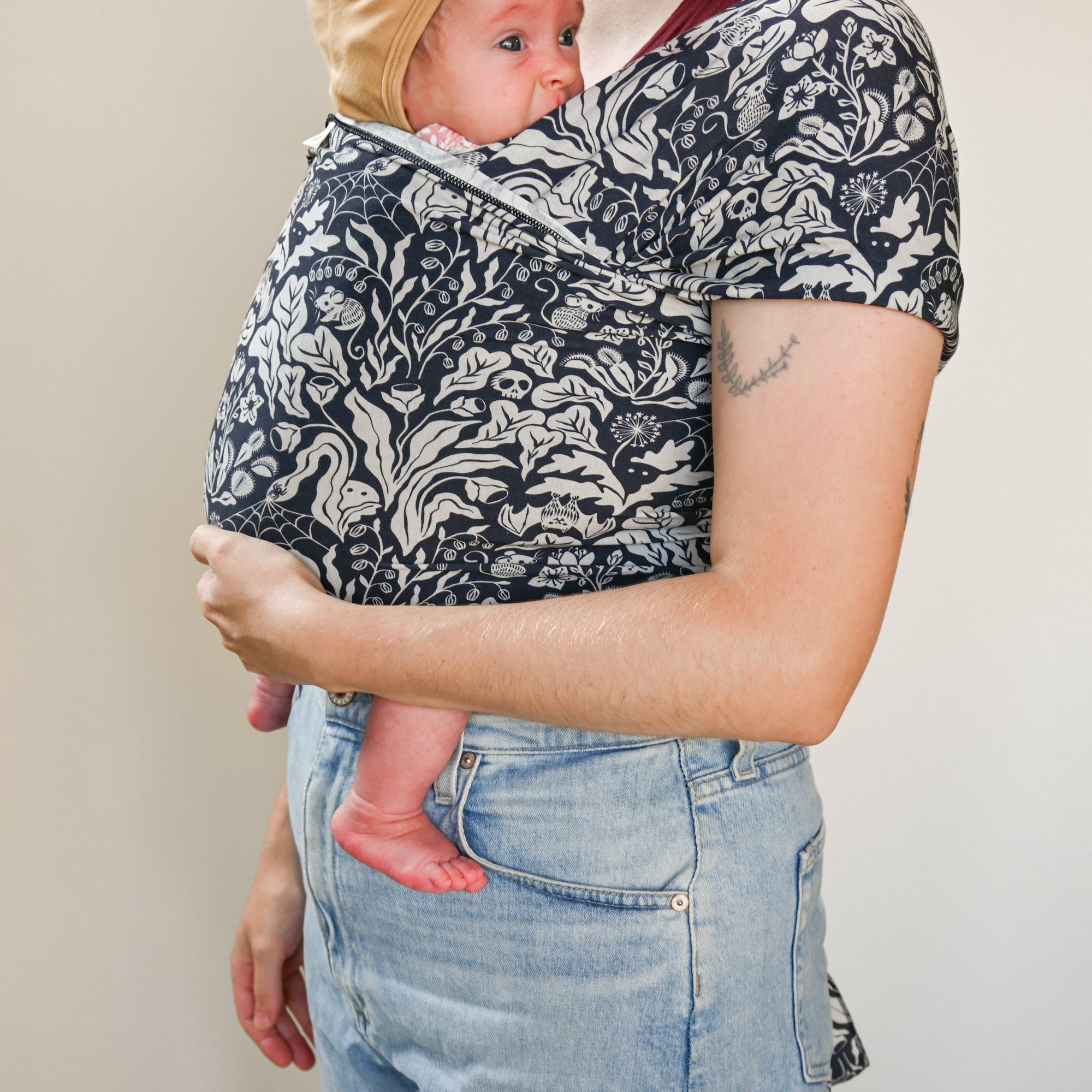 Person holding a baby in a floral-patterned sling against a neutral background