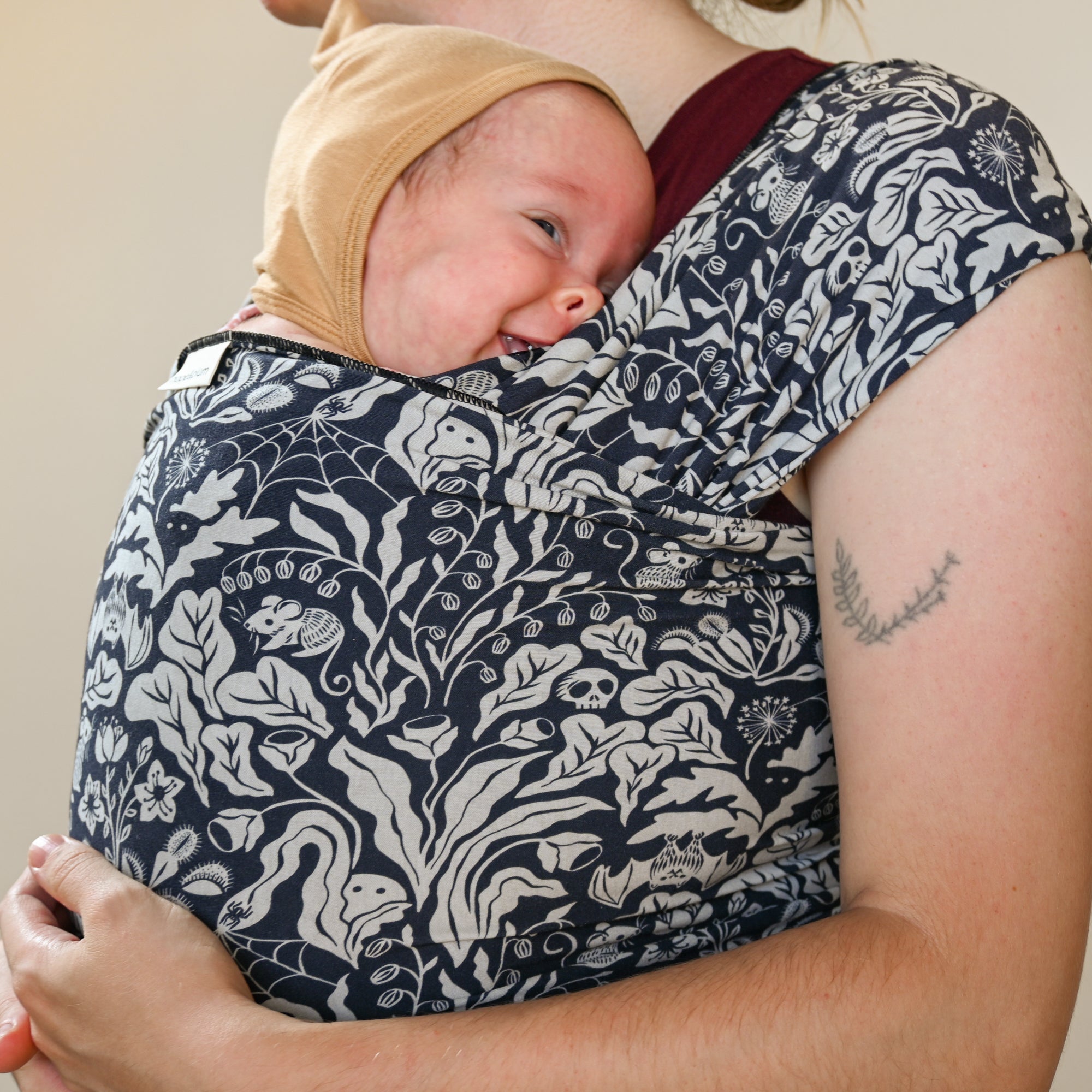 Person holding a baby in a floral-patterned sling against a neutral background