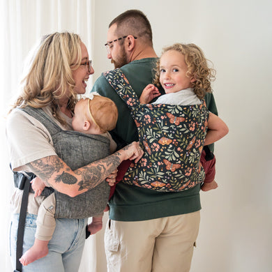 Husband and wife carrying their baby and toddler in the lark baby carrier on their front and back. 