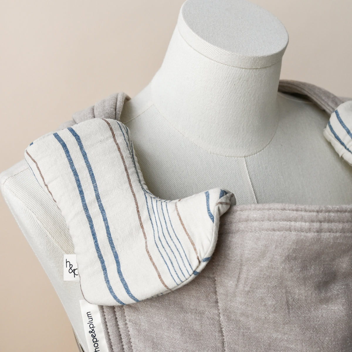 Drool Pads in Lugano, wrapped over a carrier shoulder strap on a dress form, cream woven chambray with blue stripes and fine rust pinstripes.