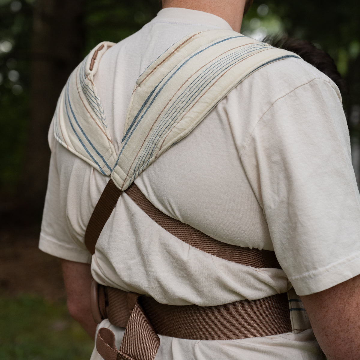 Back view of the Lugano Lark Baby Carrier showing the padded striped shoulder panels crossed above tan webbing straps.