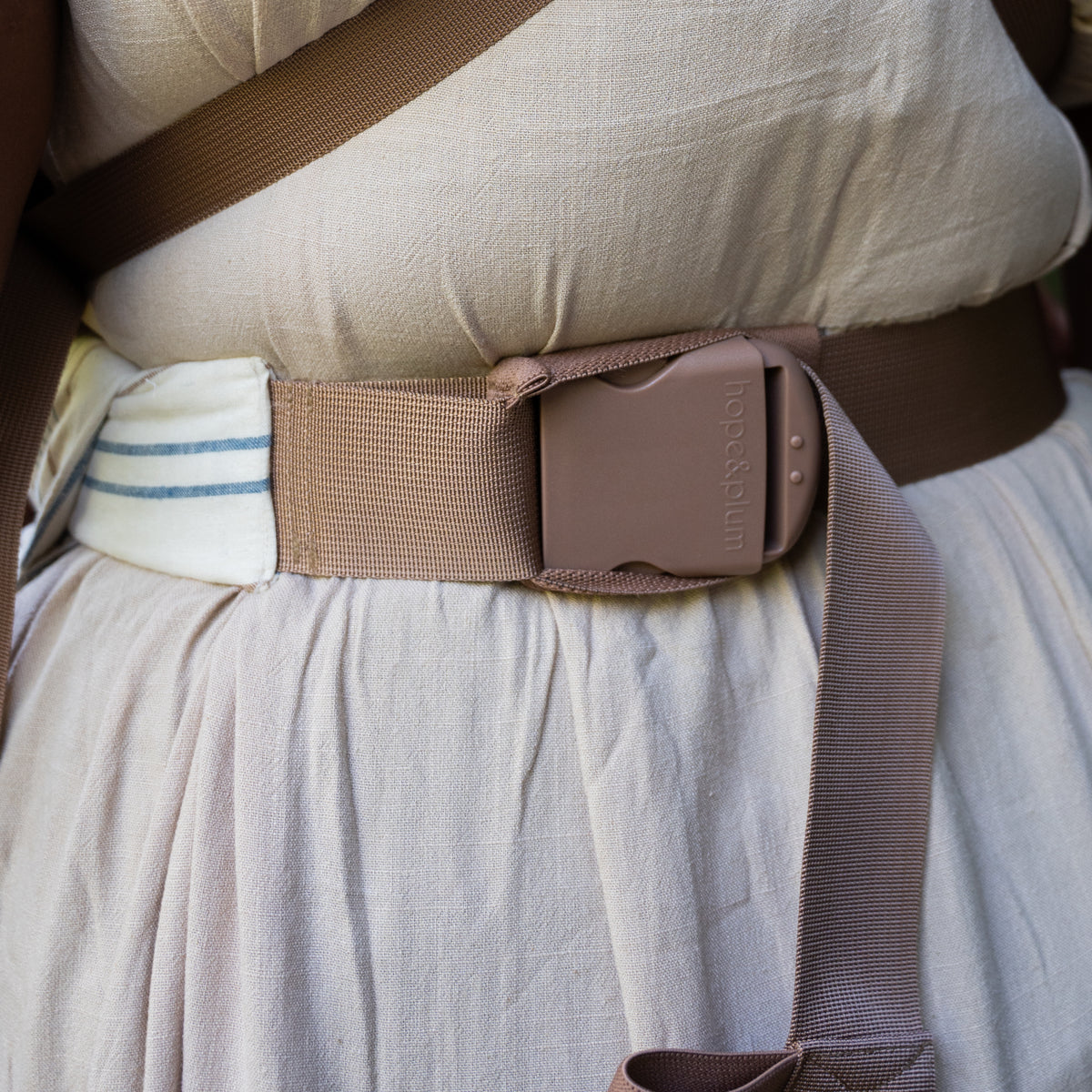 Close view of the Lugano Lark Kid Carrier's padded waistband and tan hope&plum buckle, with the striped chambray panel beside it.