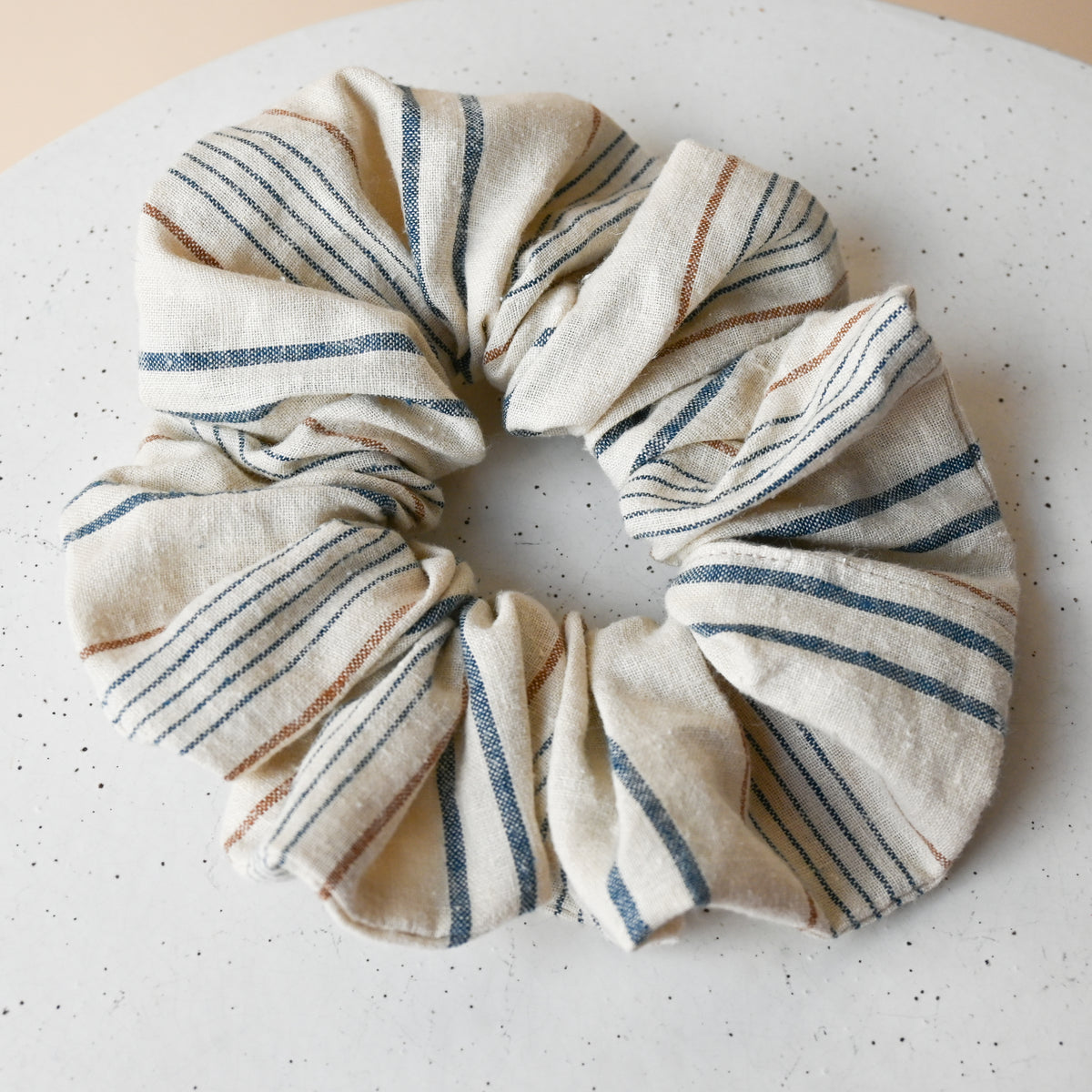 A single oversized scrunchie in Lugano, gathered into a full, voluminous ring, cream woven chambray with blue stripes and fine rust pinstripes.