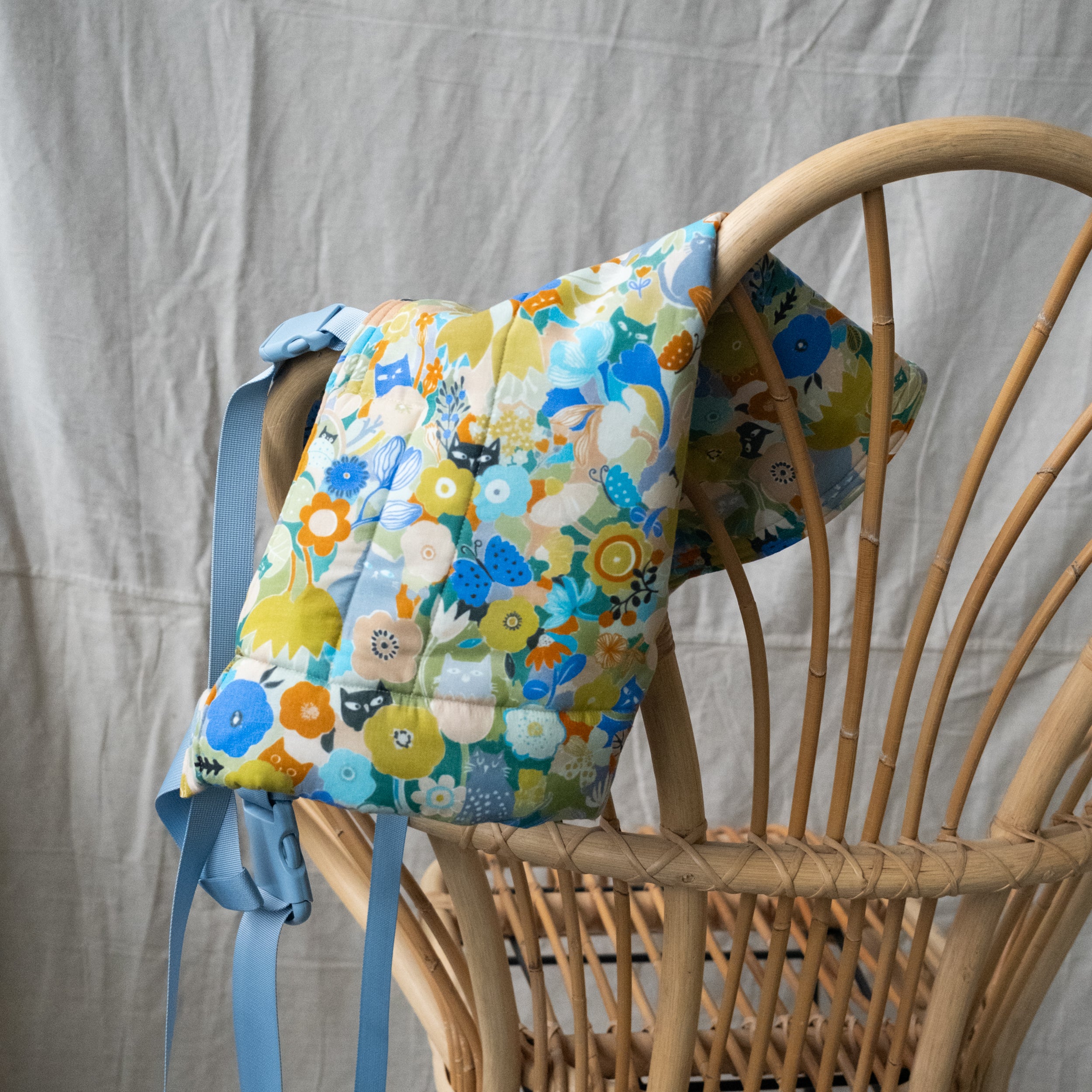 Floral-patterned Lark Buckle Carrier with blue straps on a wicker chair against a neutral background