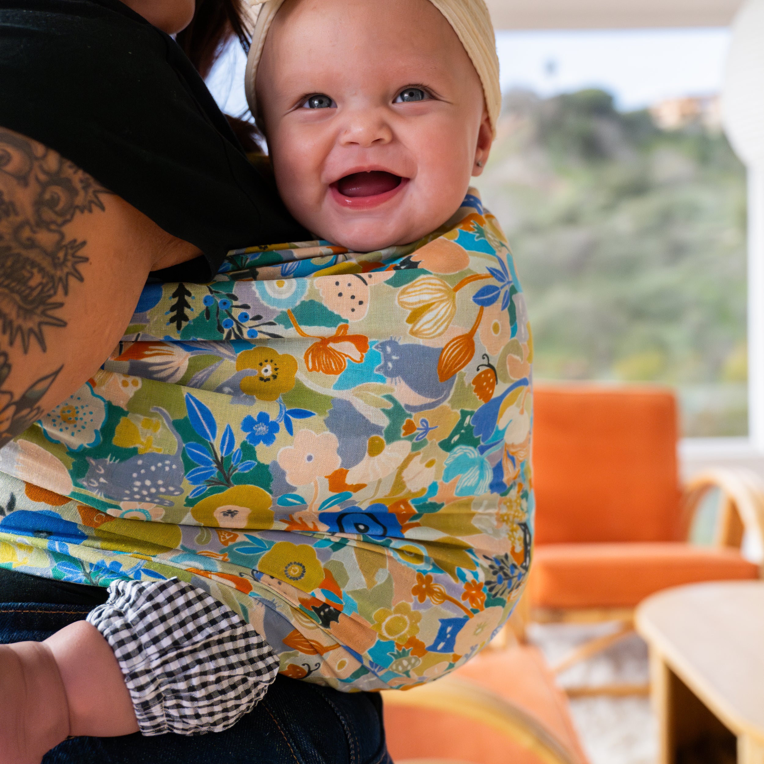 Baby in a colorful floral print ring sling with a blurred outdoor background