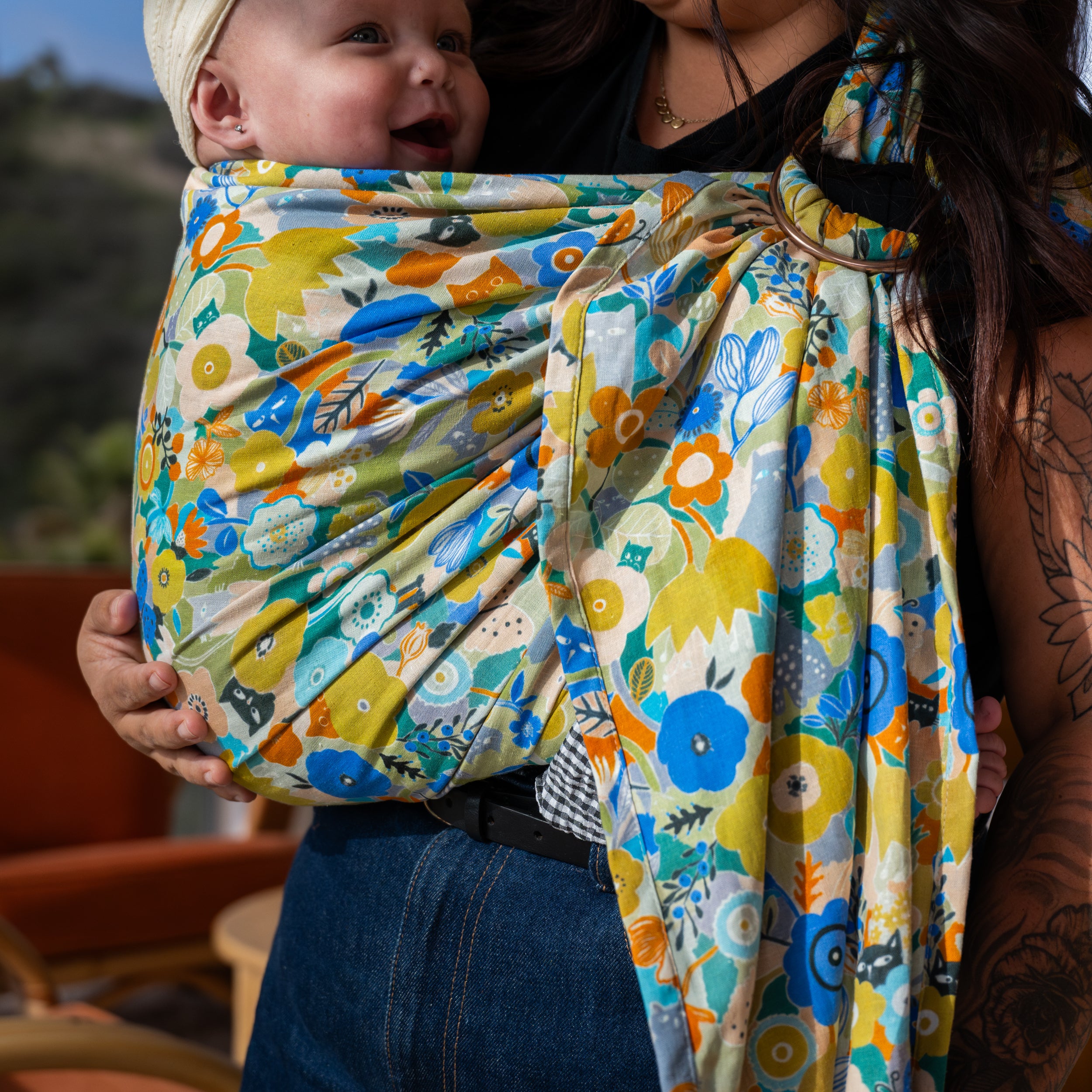 Baby in a colorful floral baby ring sling with a tattooed arm visible