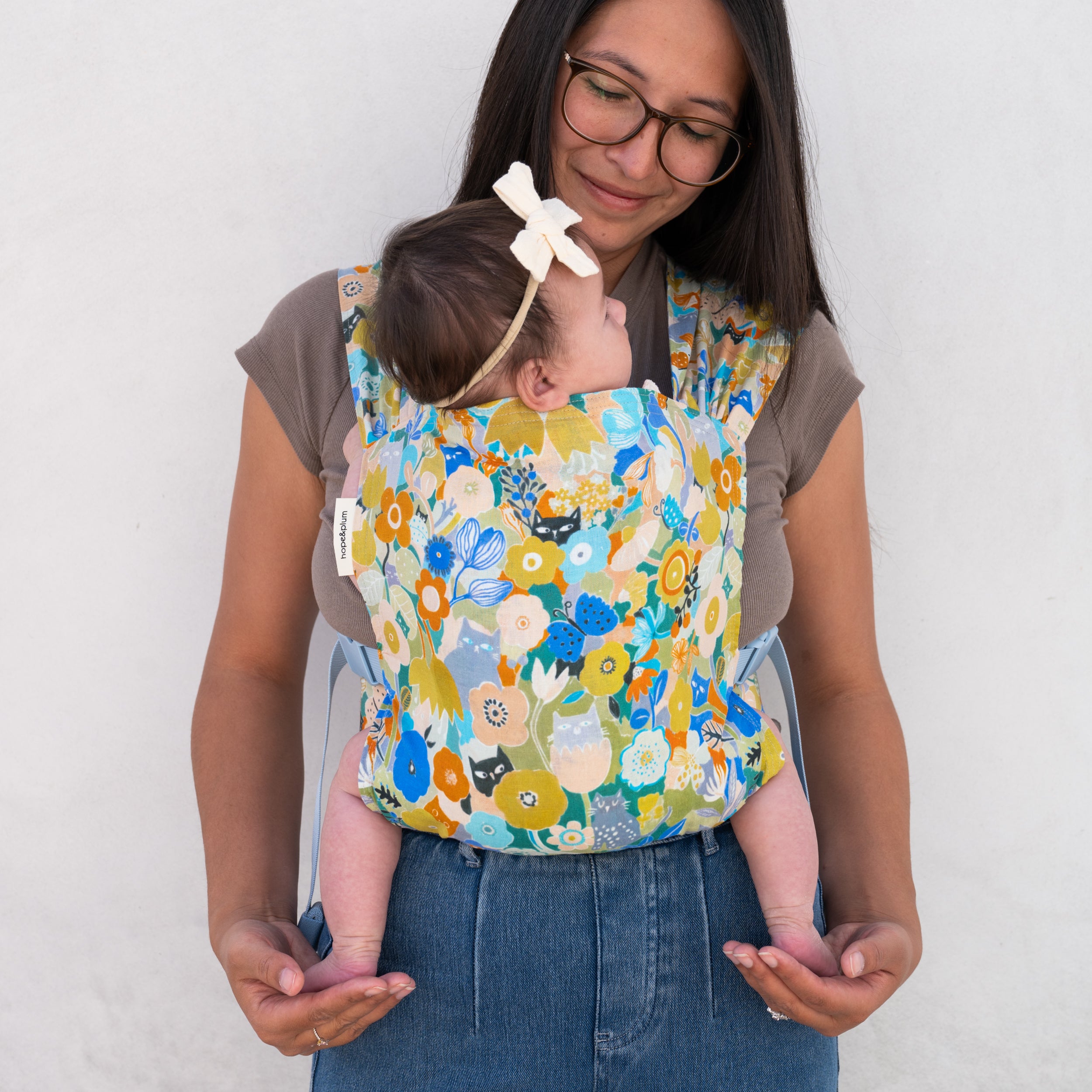 Woman holding a baby in a floral baby carrier against a white background