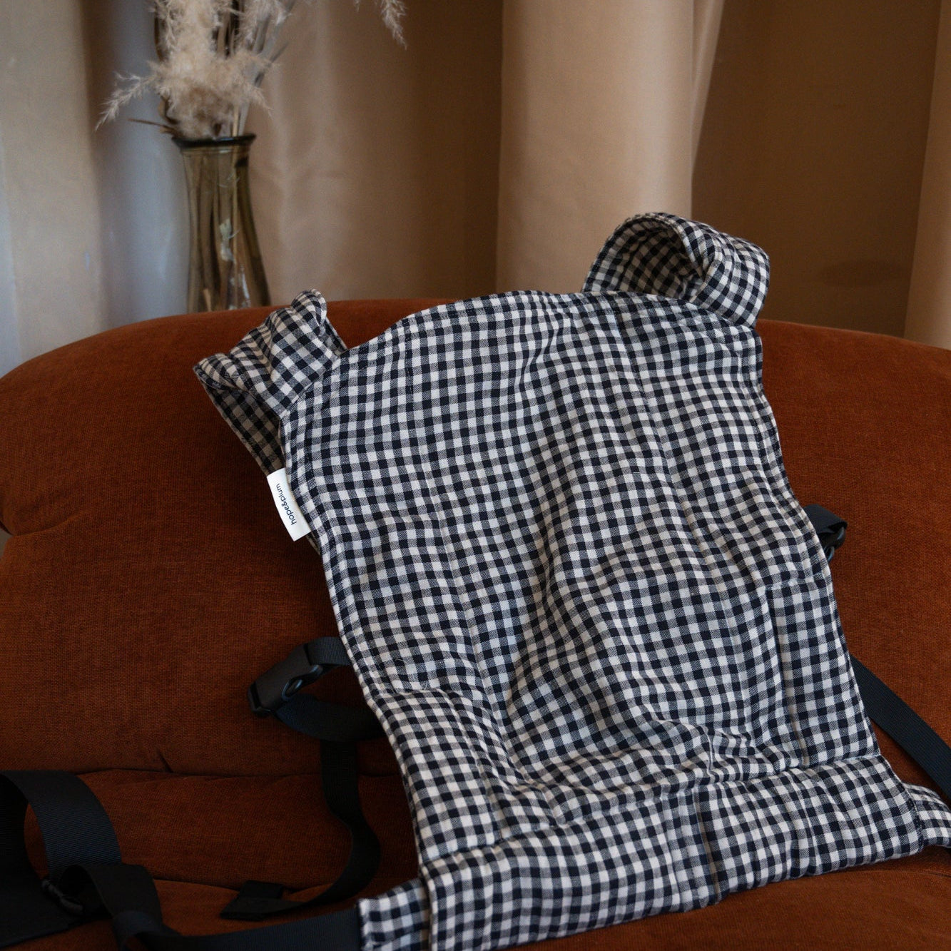Black and white checkered baby carrier on a brown couch with a neutral background