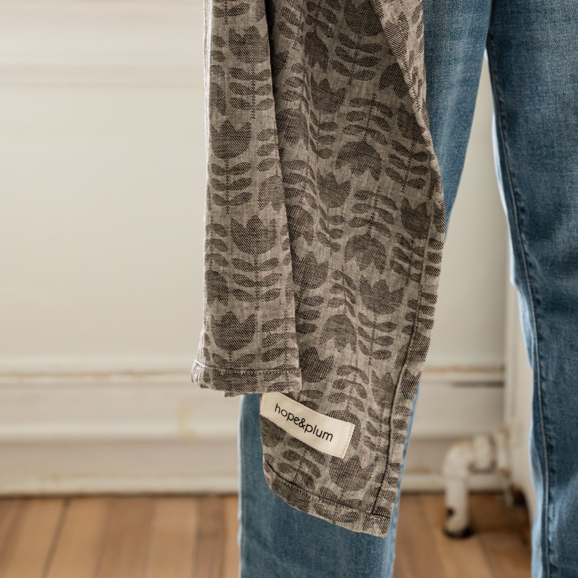 Woman holding a baby in a grey tulip patterned ring sling against a neutral background