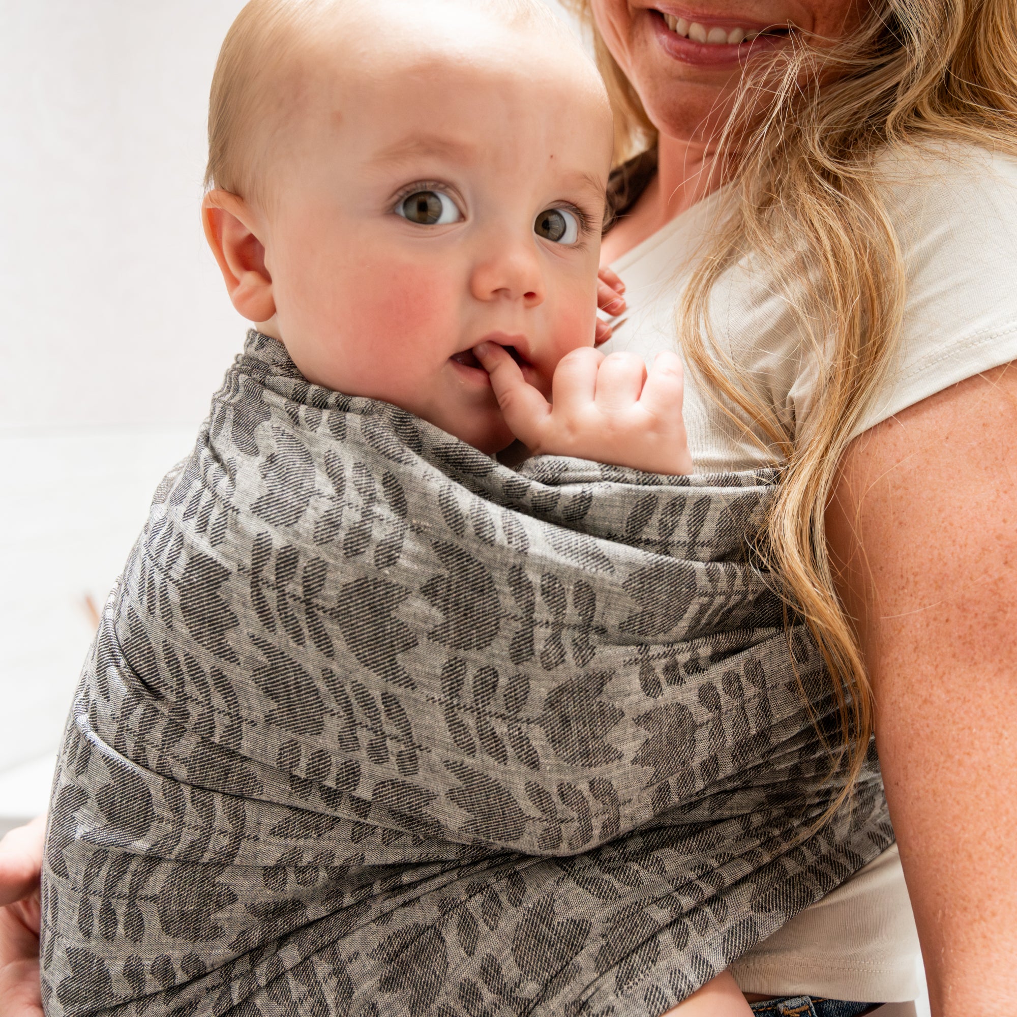 Woman holding a baby in a grey tulip patterned ring sling against a neutral background