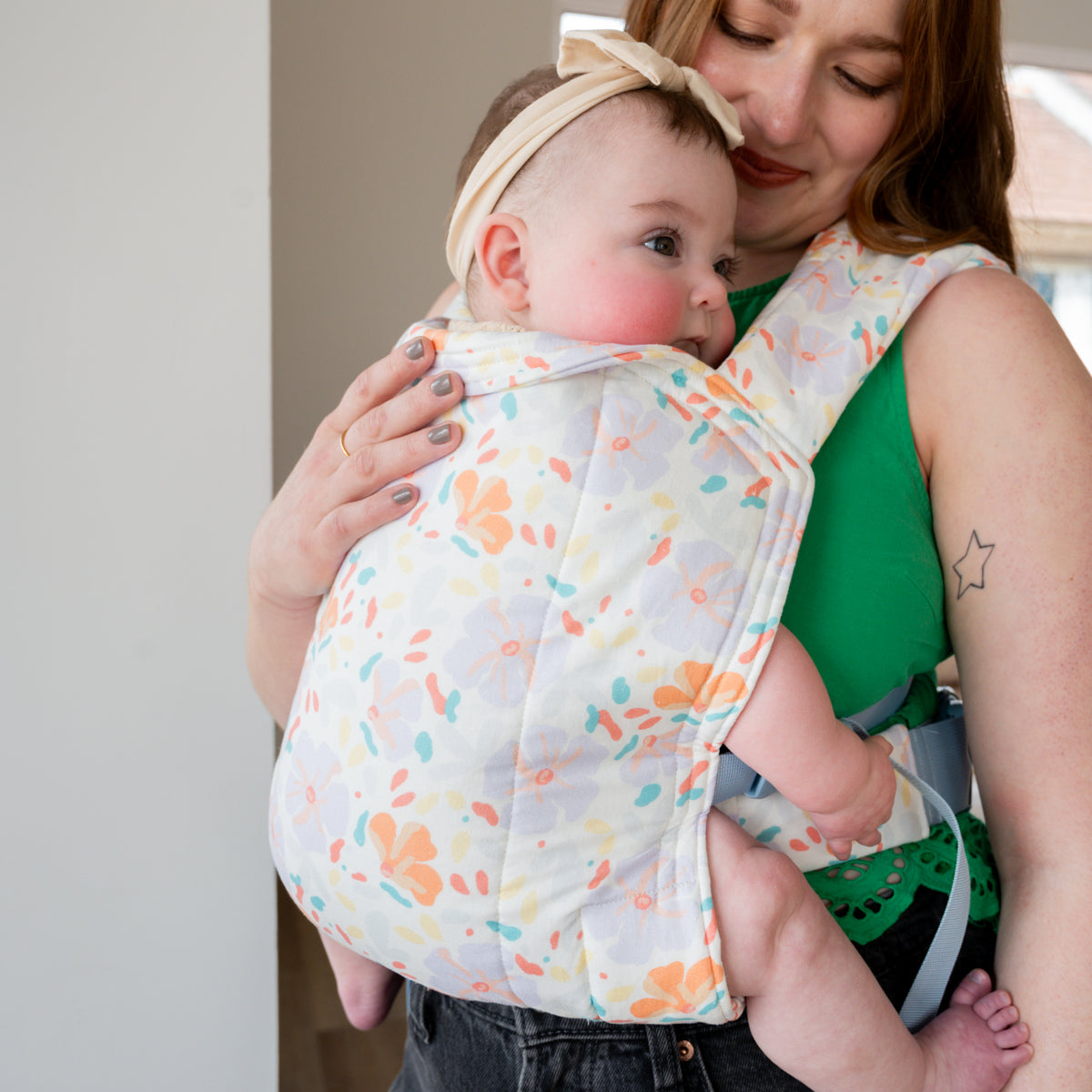 A caregiver nuzzles a rosy-cheeked baby in the Petal Lark — a cream woven fabric with an abstract scatter of peach, teal, yellow, and lavender petal shapes.