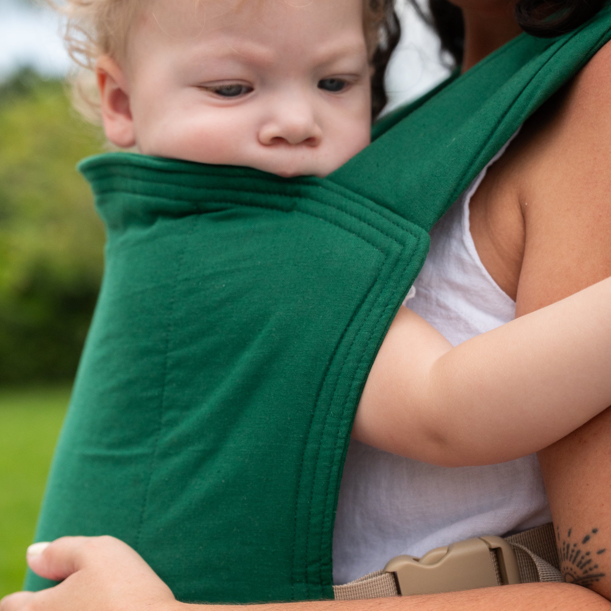 Child being carried in a green baby carrier with a blurred natural background