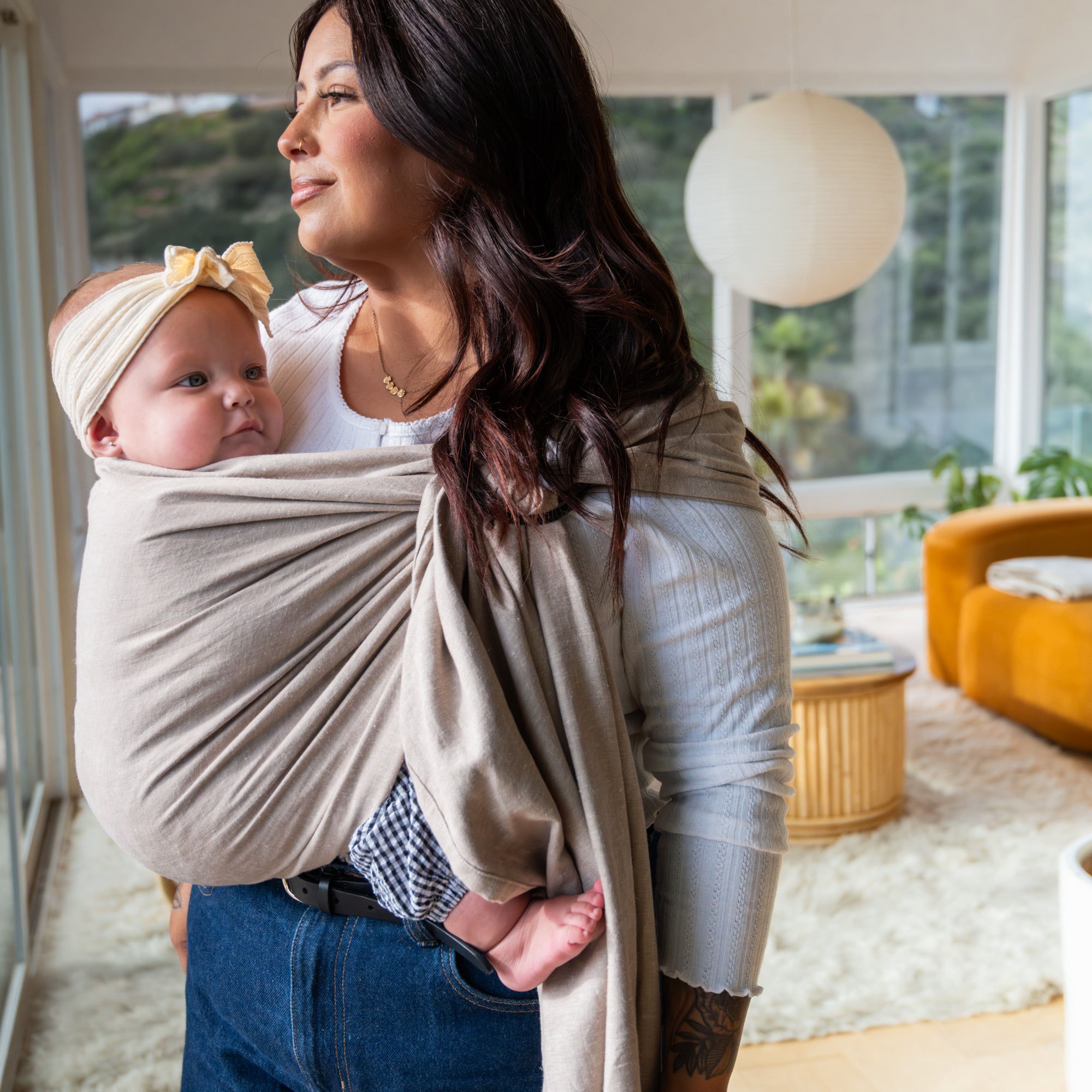 Woman holding a baby in a beige sling in a living room setting