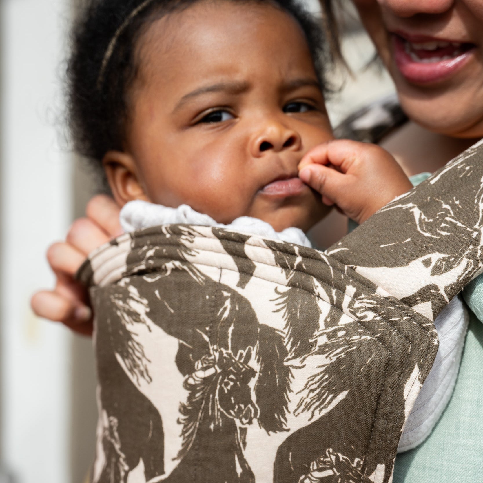 Lark Baby Carrier in Rodeo — close-up of a toddler resting against the quilted hood in the mustang print.