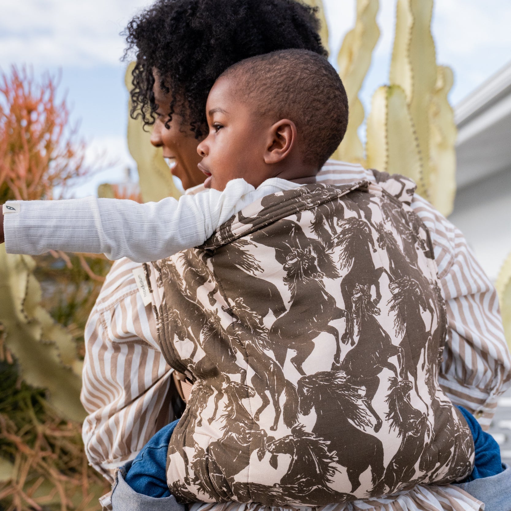 Lark Kid Carrier in Rodeo — caregiver and toddler both looking outward, toddler carried in the mustang print.