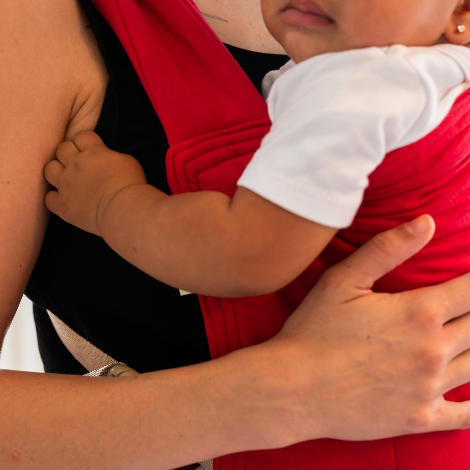 Person holding a child wearing a red buckle baby carrier.