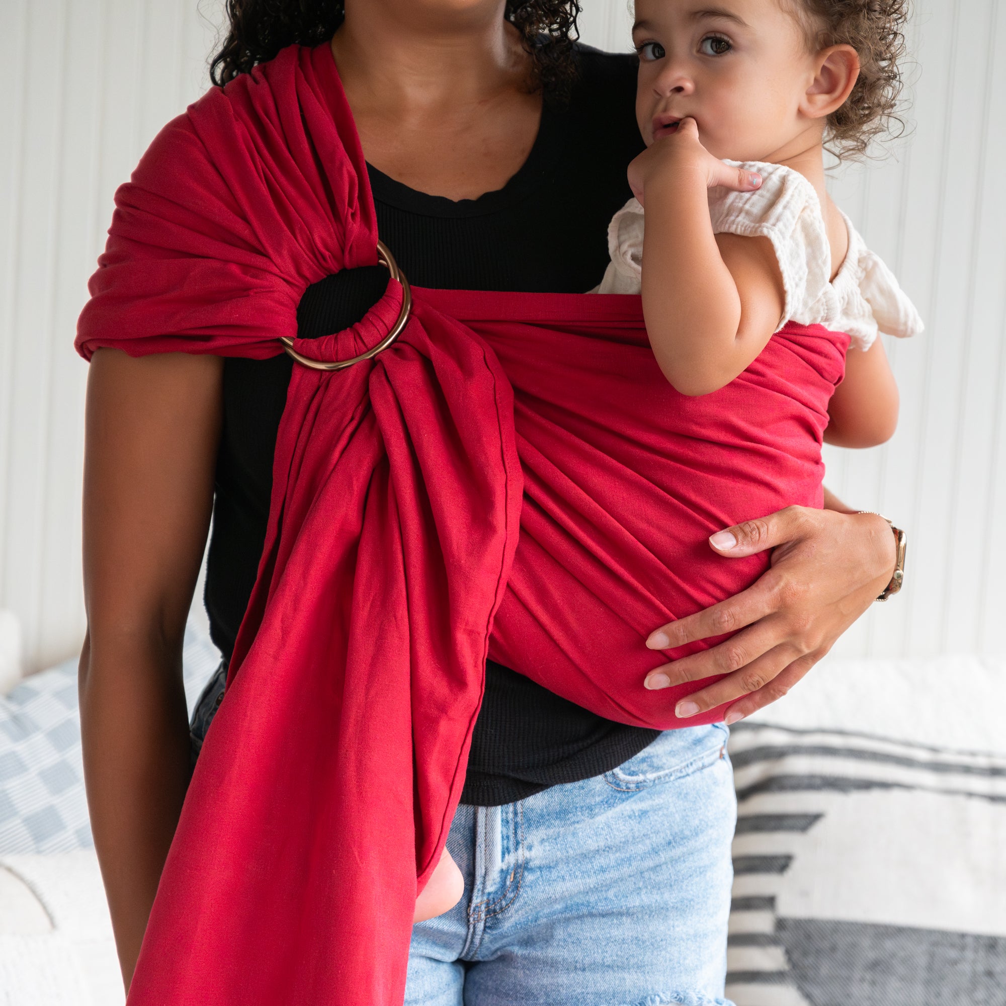 Woman holding a child in a red baby wrap against a neutral background
