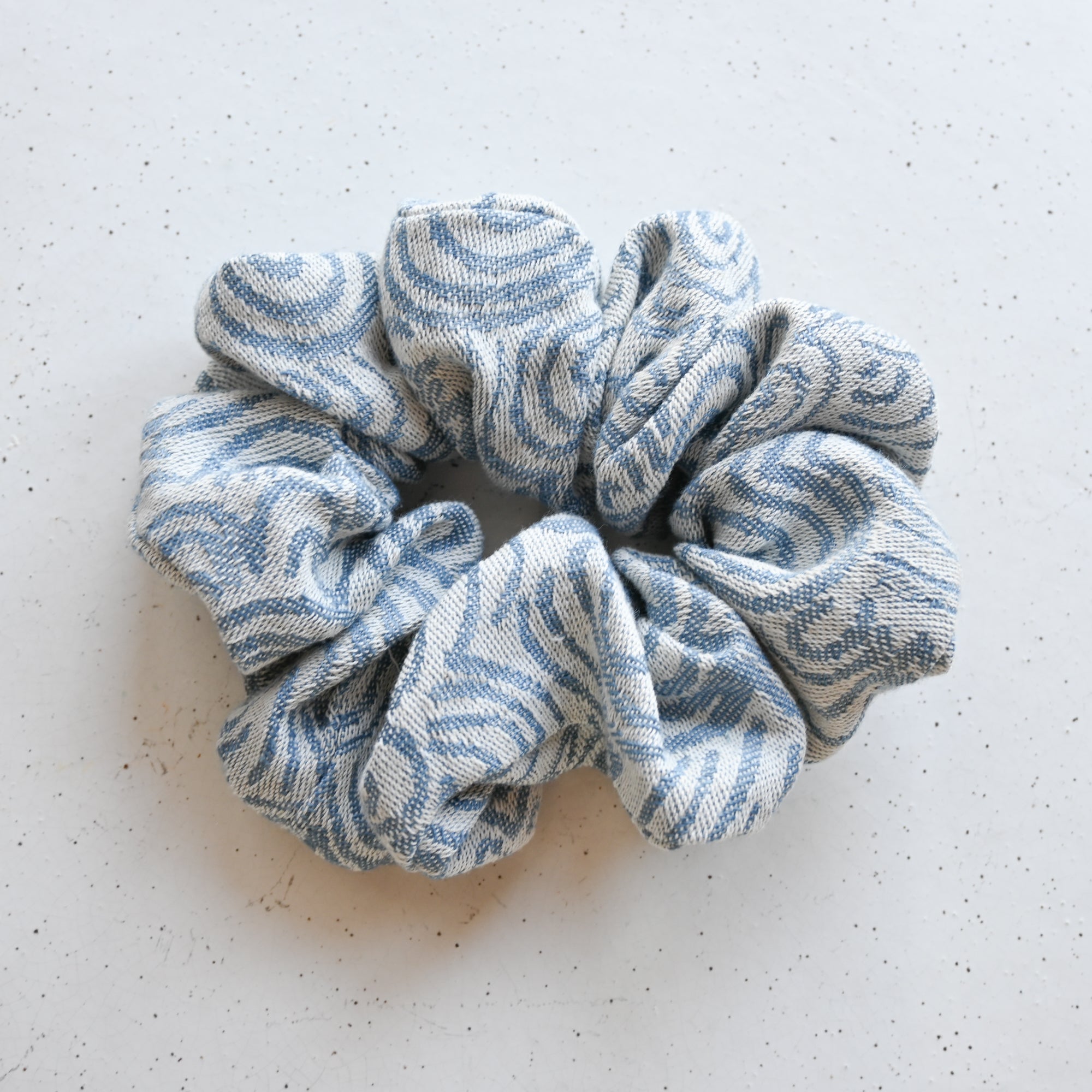 A single oversized scrunchie in cream woven fabric with a dusty blue wave pattern in a jacquard-style weave.